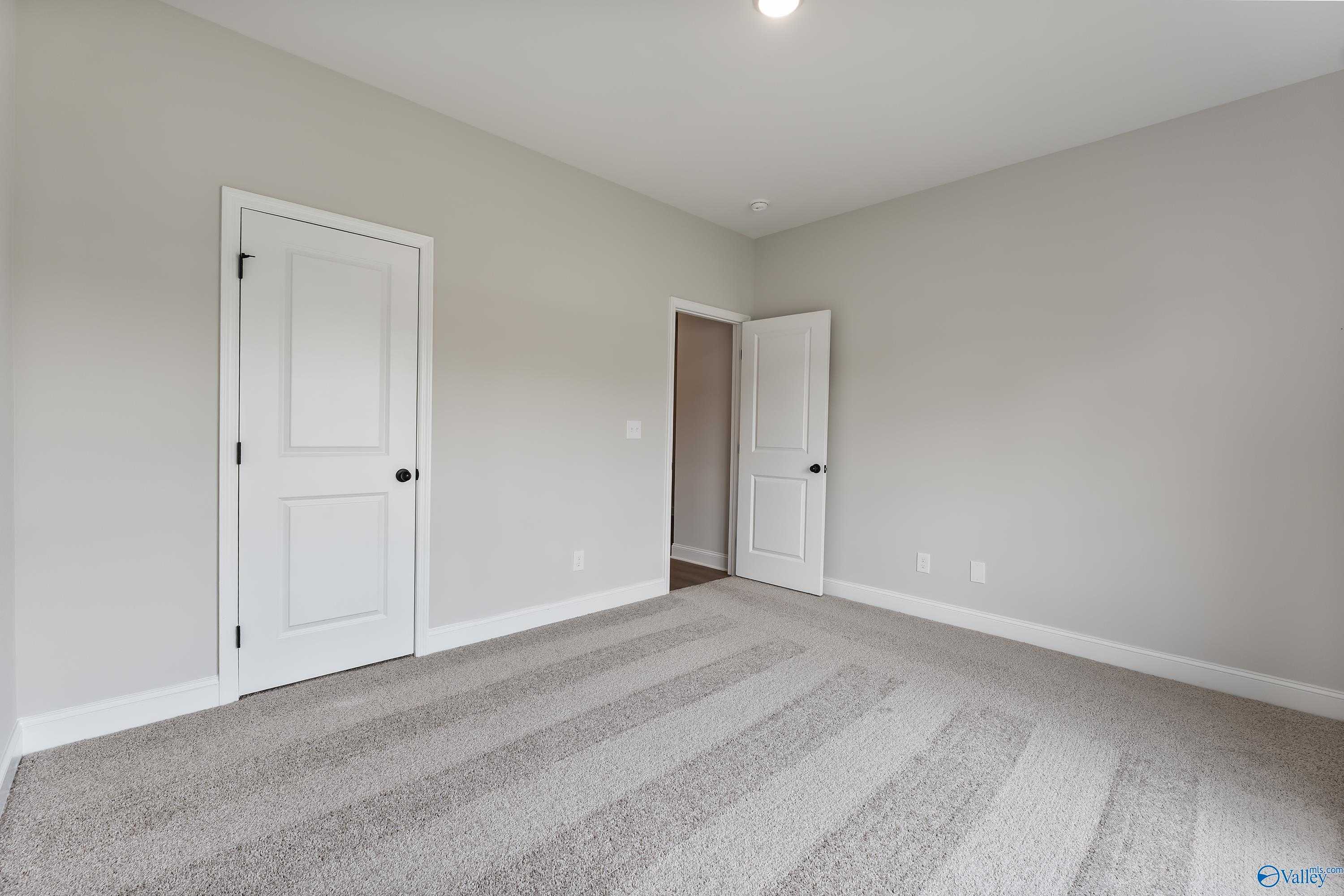 Empty secondary bedroom with light gray walls, white doors, and neutral carpet in The Daphne 4-bedroom home, Huntsville, AL
