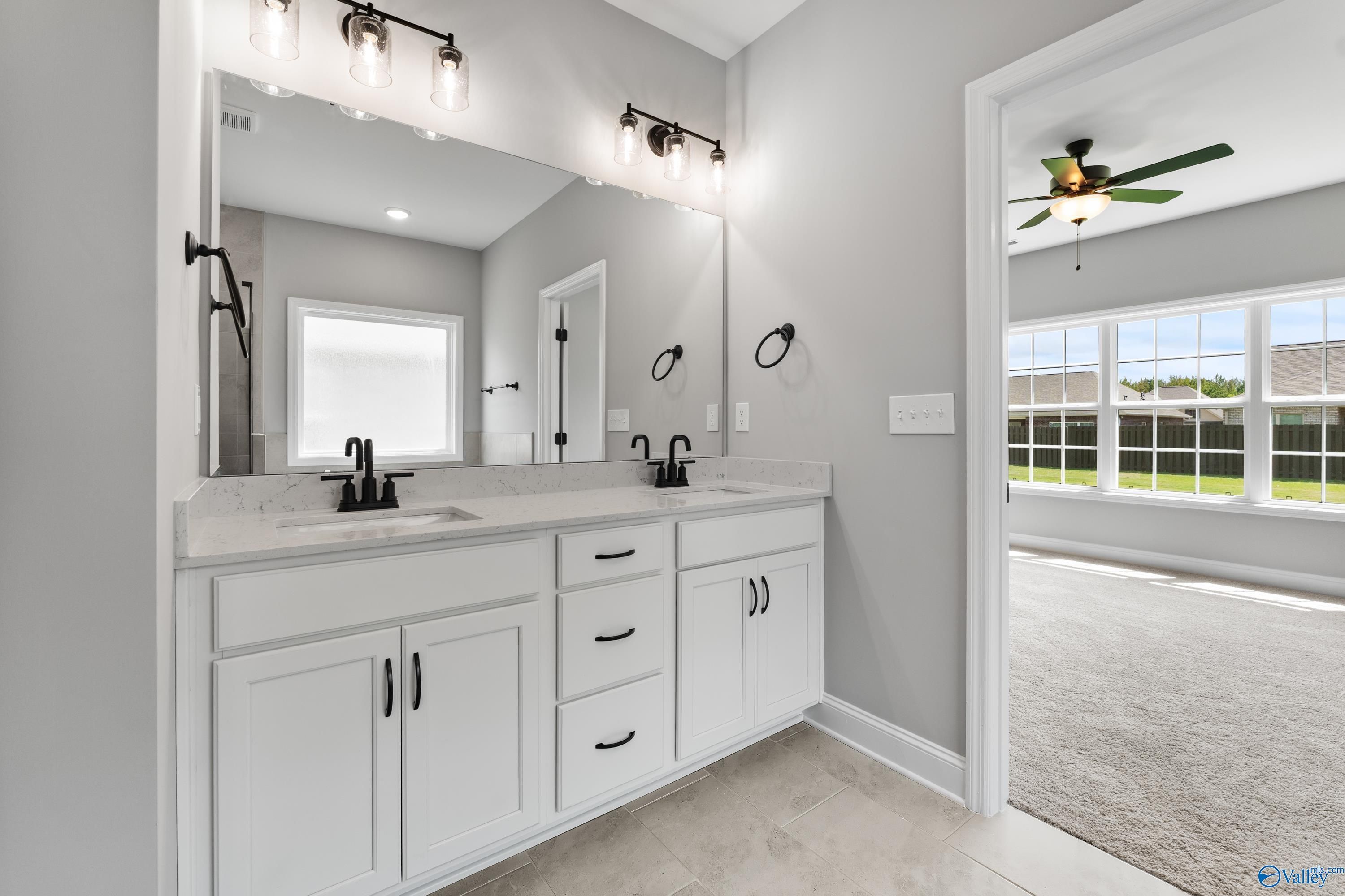 Modern master bathroom with double white vanity, black hardware, large mirrors, and gray walls in Davidson Homes Montgomery B, Toney, Alabama
