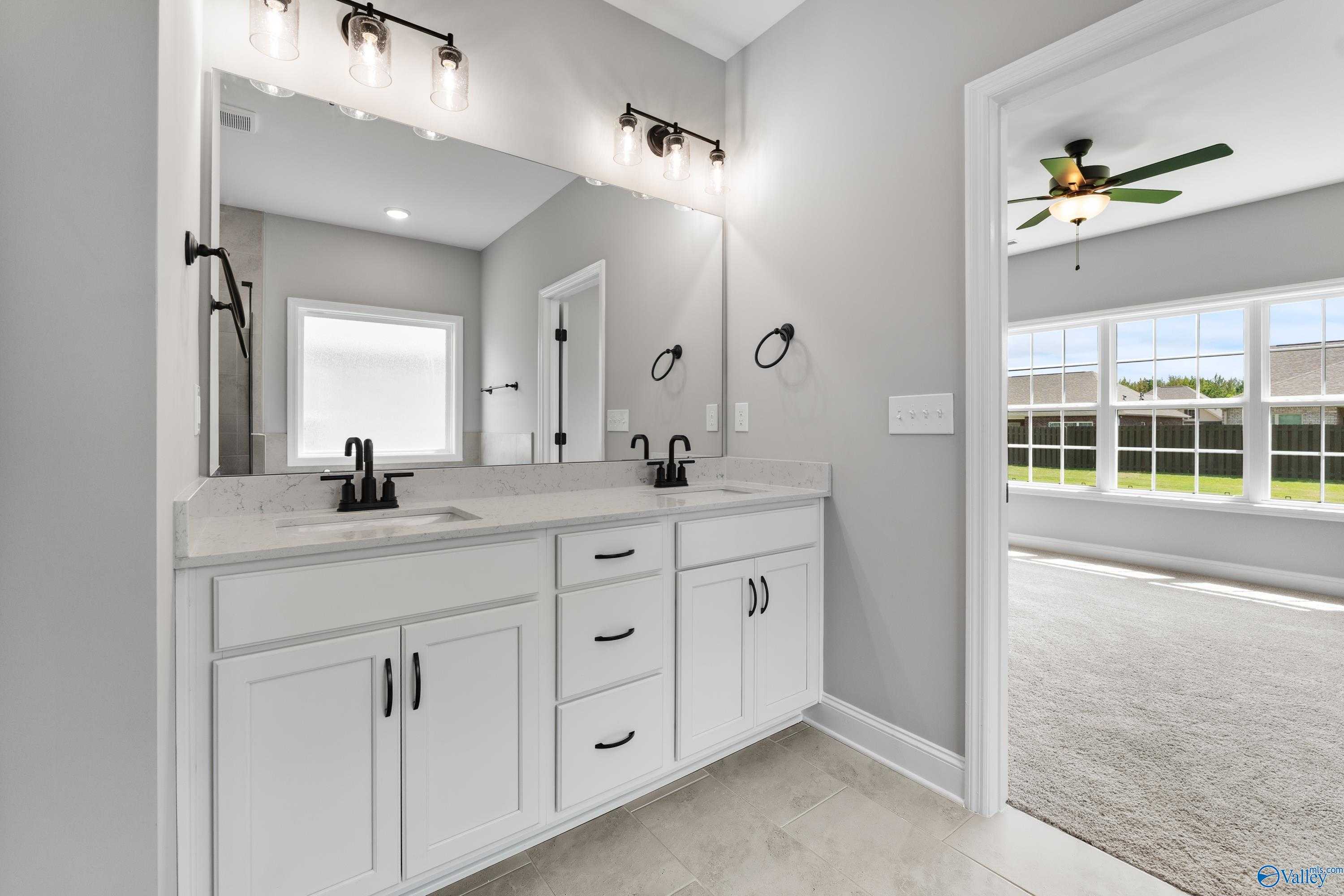 Modern master bathroom with double white vanity, black hardware, large mirrors, and gray walls in Davidson Homes Montgomery B, Toney, Alabama