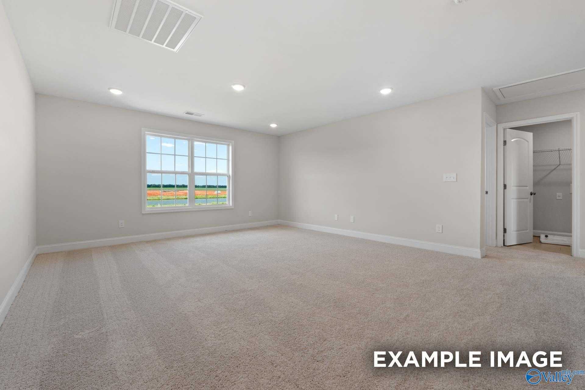 Spacious empty bedroom with large sunny window, carpeted floors, and en-suite bath door in The Madison A 5-bedroom home, Meridianville, Alabama
