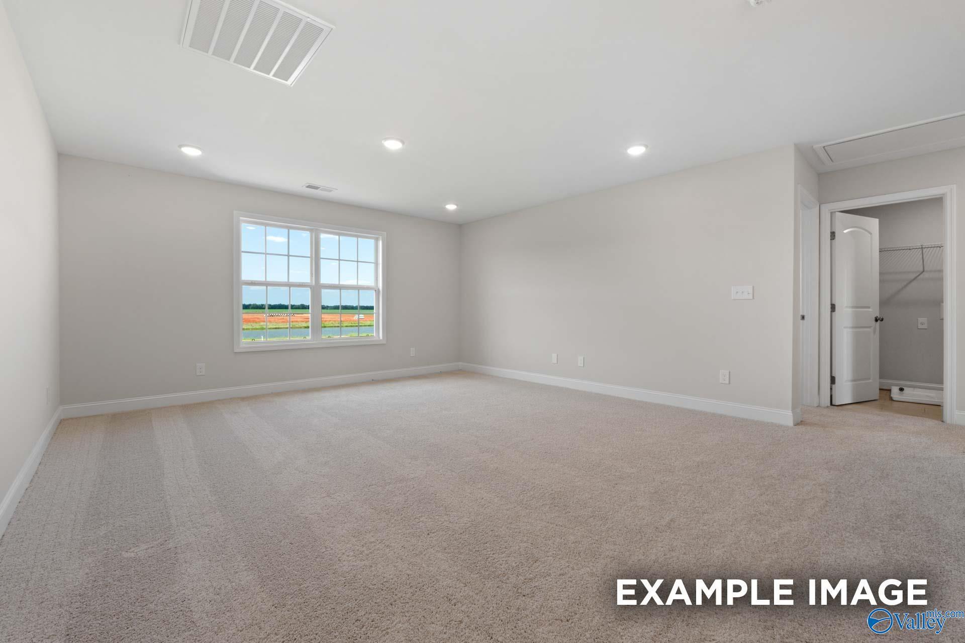 Spacious empty bedroom with beige carpet, light gray walls, large window to green fields, open walk-in closet in Davidson Homes Madison A, Meridianville AL