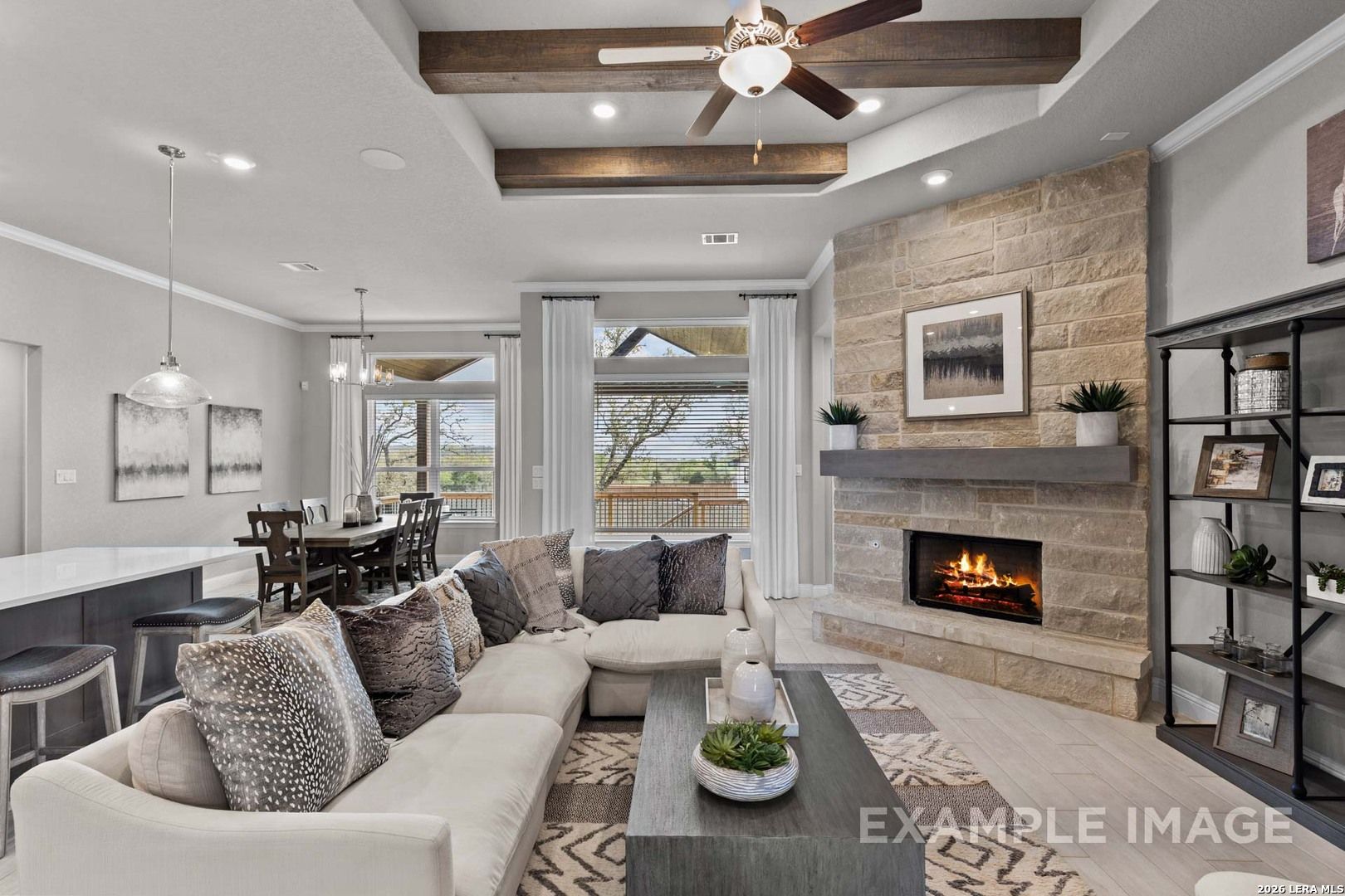 Open-concept living room with stone fireplace, wood beam ceiling, and dining area in The Garner C home, Castroville, TX.