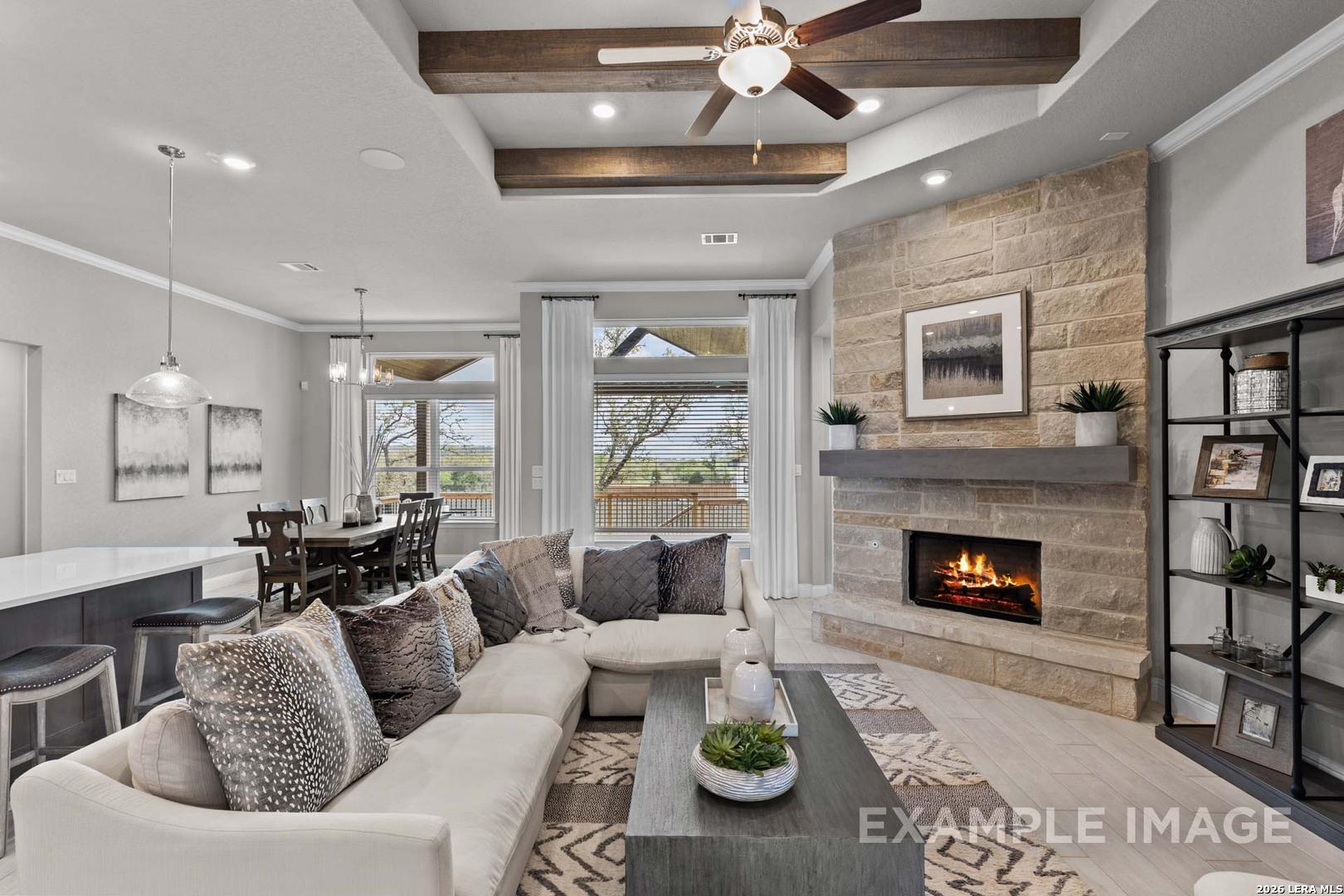 Open-concept living room with stone fireplace, wood beam ceiling, and dining area in The Garner C home, Castroville, TX.