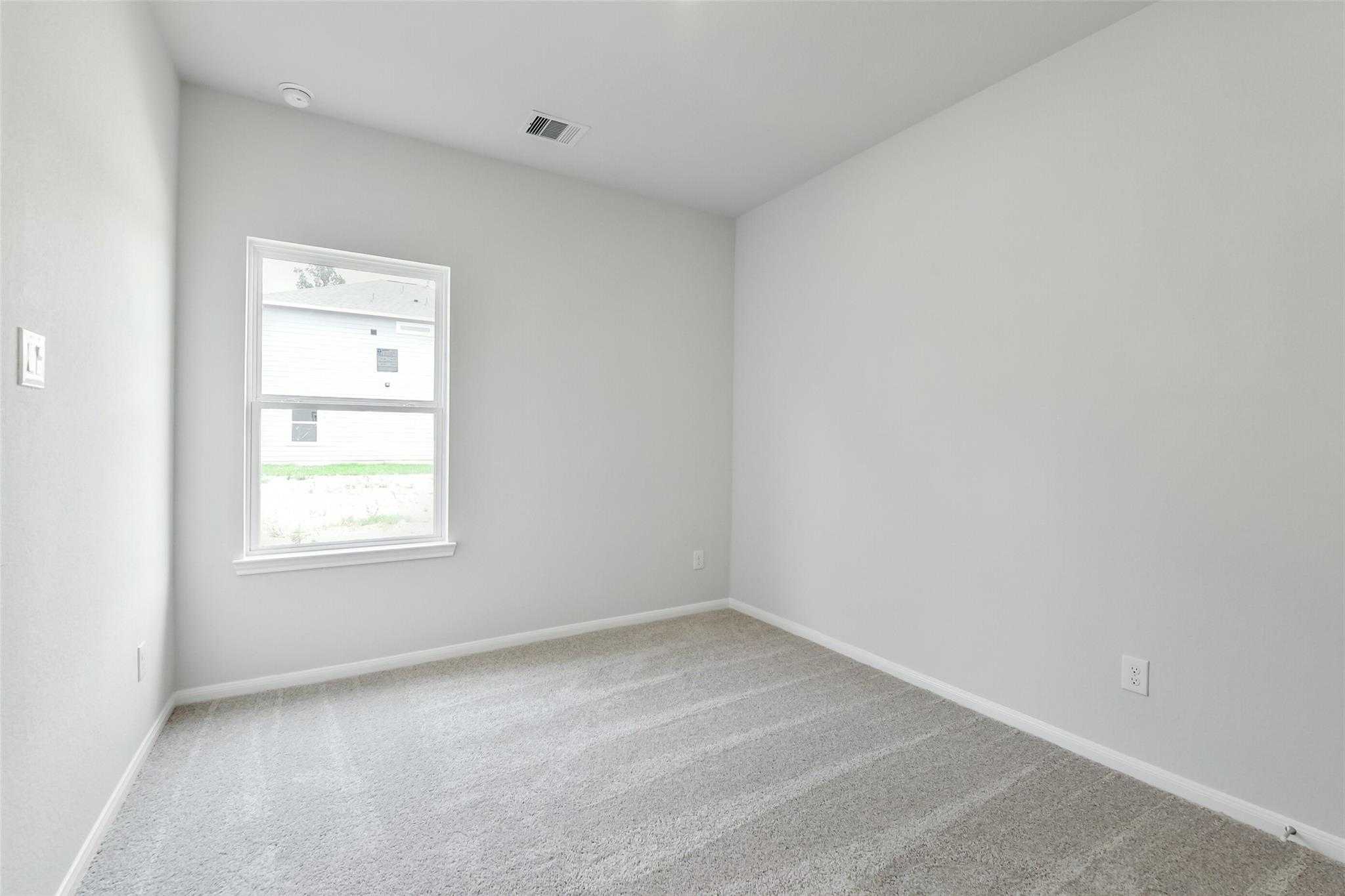Bright secondary bedroom with gray walls, beige carpet, and window overlooking lawn in Davidson Homes Sabine E, Conroe TX