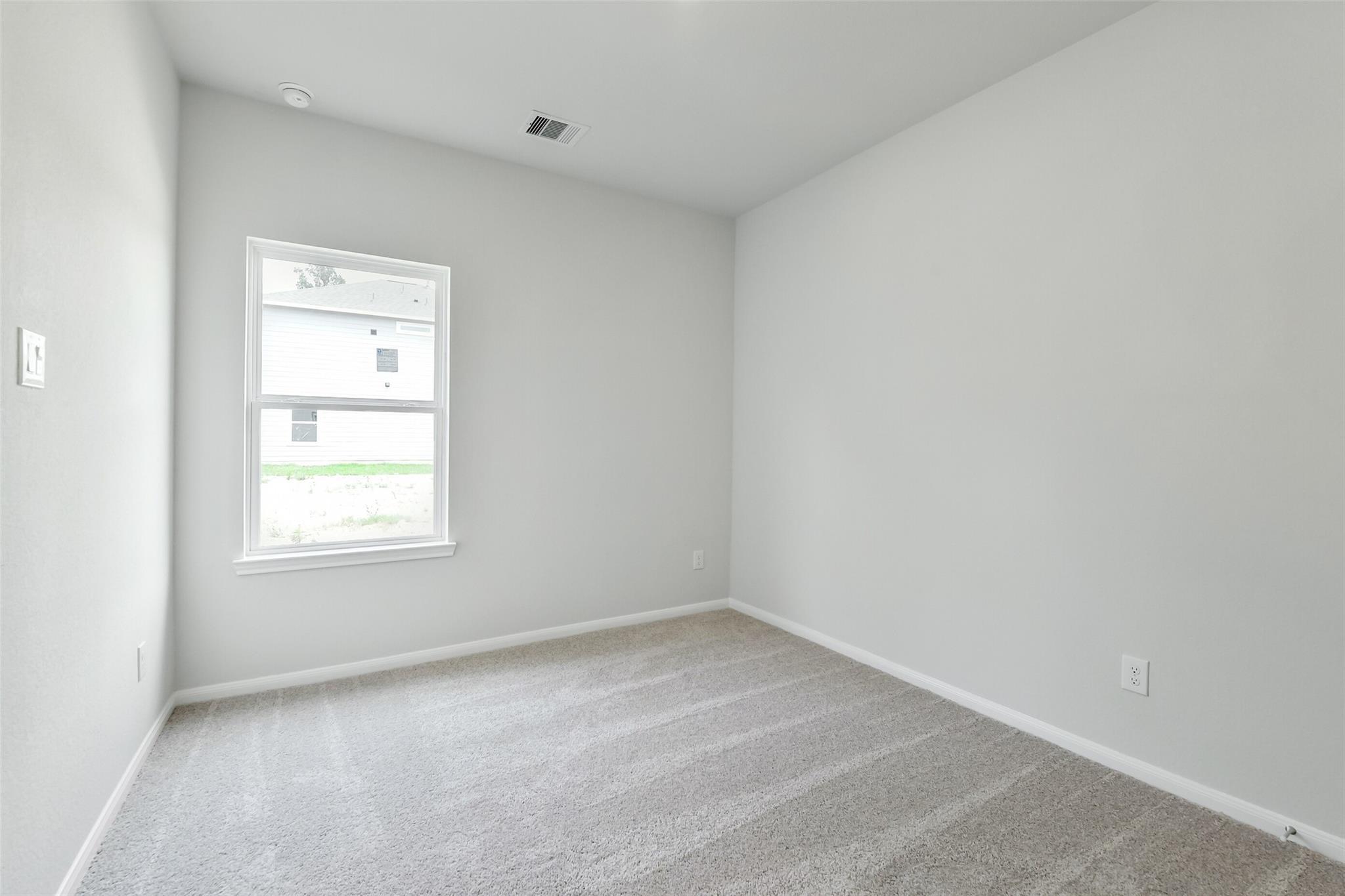 Bright secondary bedroom with gray walls, beige carpet, and window overlooking lawn in Davidson Homes Sabine E, Conroe TX