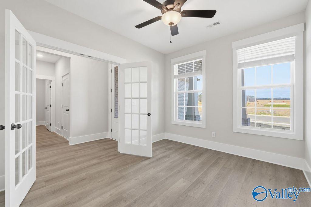 Bright room with ceiling fan, open French doors to hallway, and large windows overlooking fields in Davidson Homes The Rockford, Hartselle, Alabama