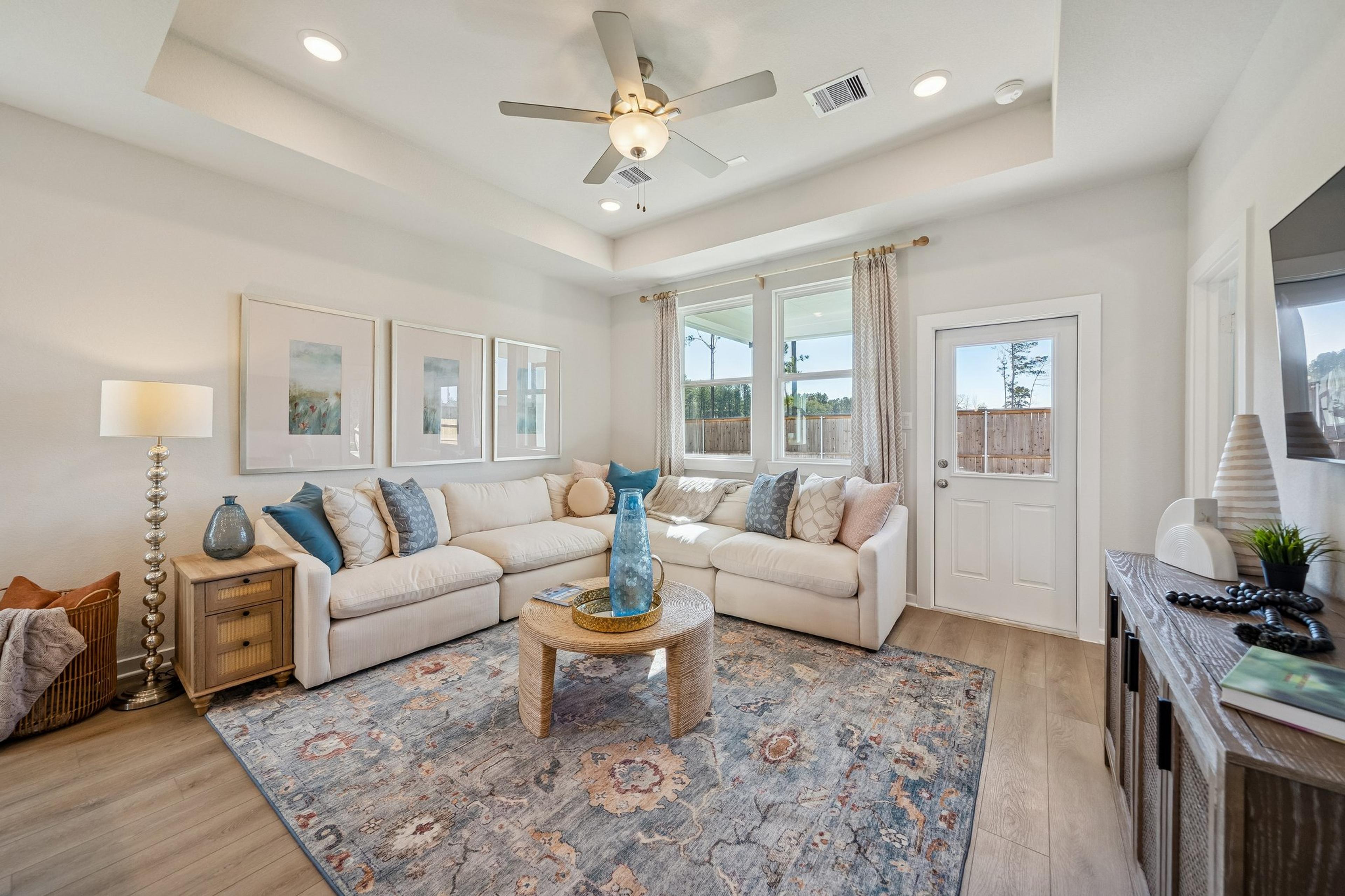 Open-concept living room and kitchen at Spring Branch Crossing in Conroe Texas featuring pink armchairs, hardwood floors, and white cabinetry
