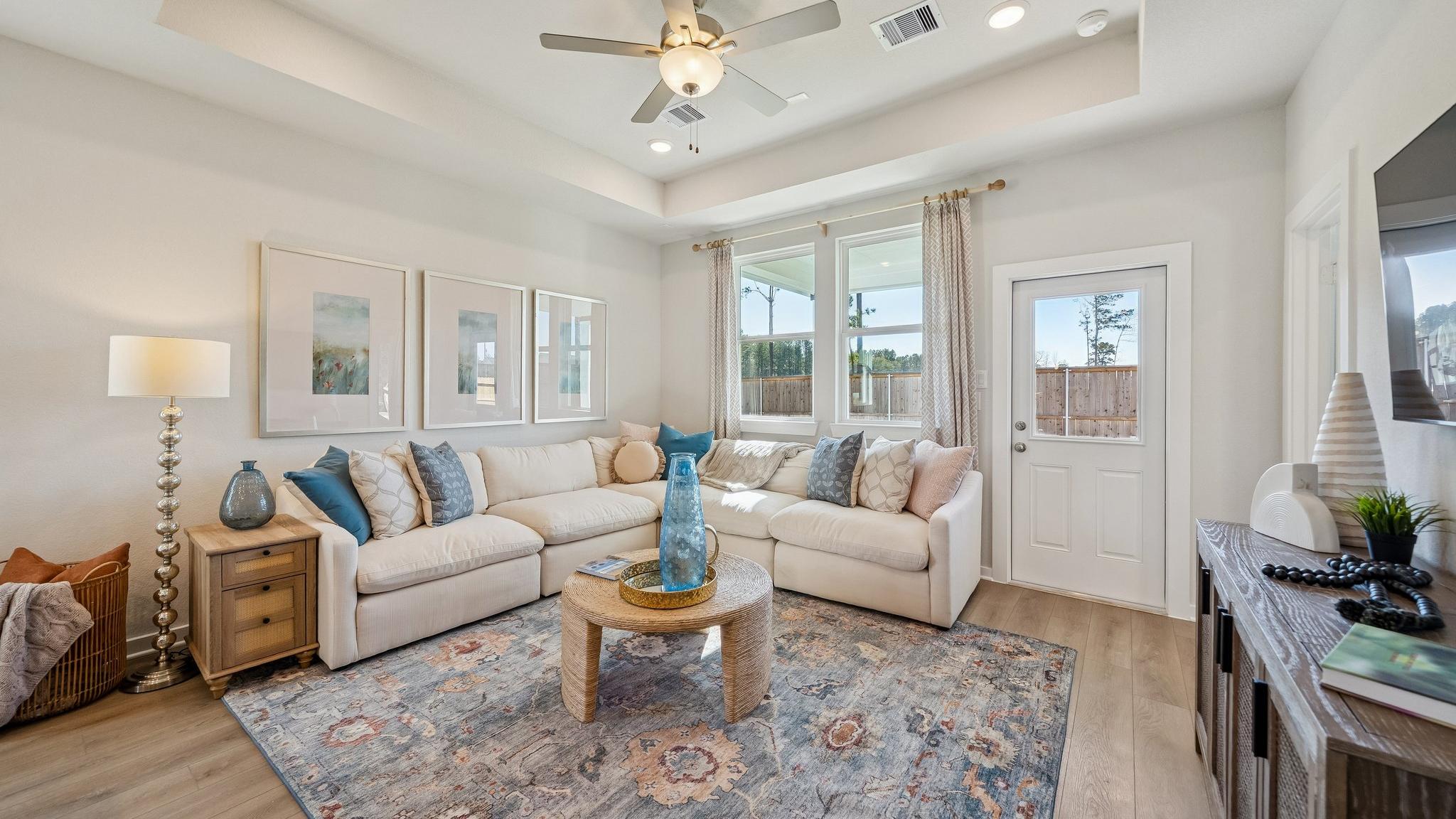 Open-concept living room and kitchen at Spring Branch Crossing in Conroe Texas featuring pink armchairs, hardwood floors, and white cabinetry