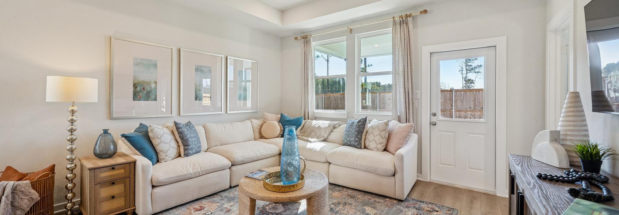 Open-concept living room and kitchen at Spring Branch Crossing in Conroe Texas featuring pink armchairs, hardwood floors, and white cabinetry