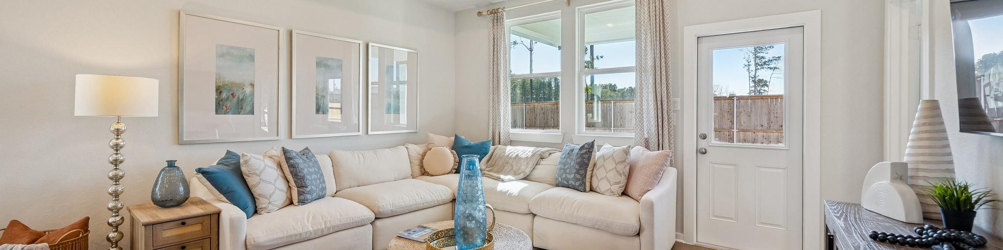 Open-concept living room and kitchen at Spring Branch Crossing in Conroe Texas featuring pink armchairs, hardwood floors, and white cabinetry