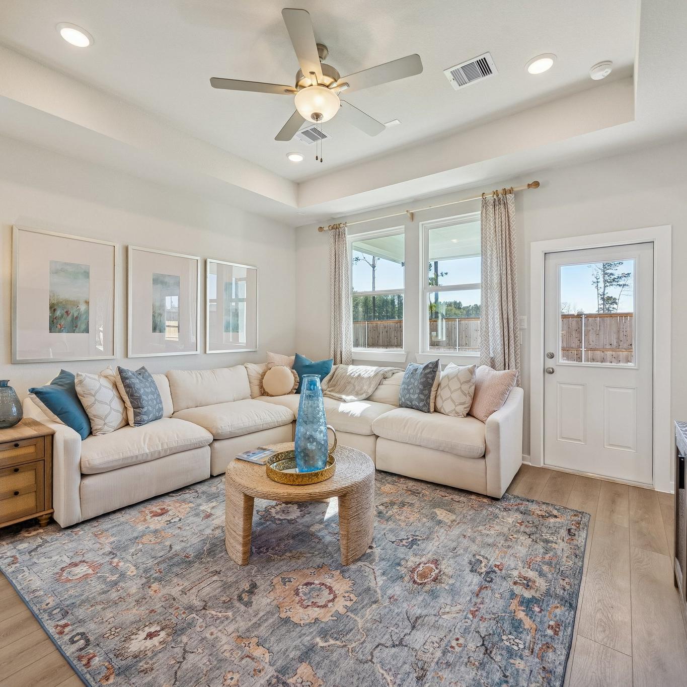 Open-concept living room and kitchen at Spring Branch Crossing in Conroe Texas featuring pink armchairs, hardwood floors, and white cabinetry
