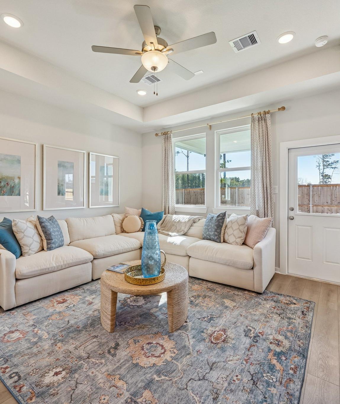 Open-concept living room and kitchen at Spring Branch Crossing in Conroe Texas featuring pink armchairs, hardwood floors, and white cabinetry