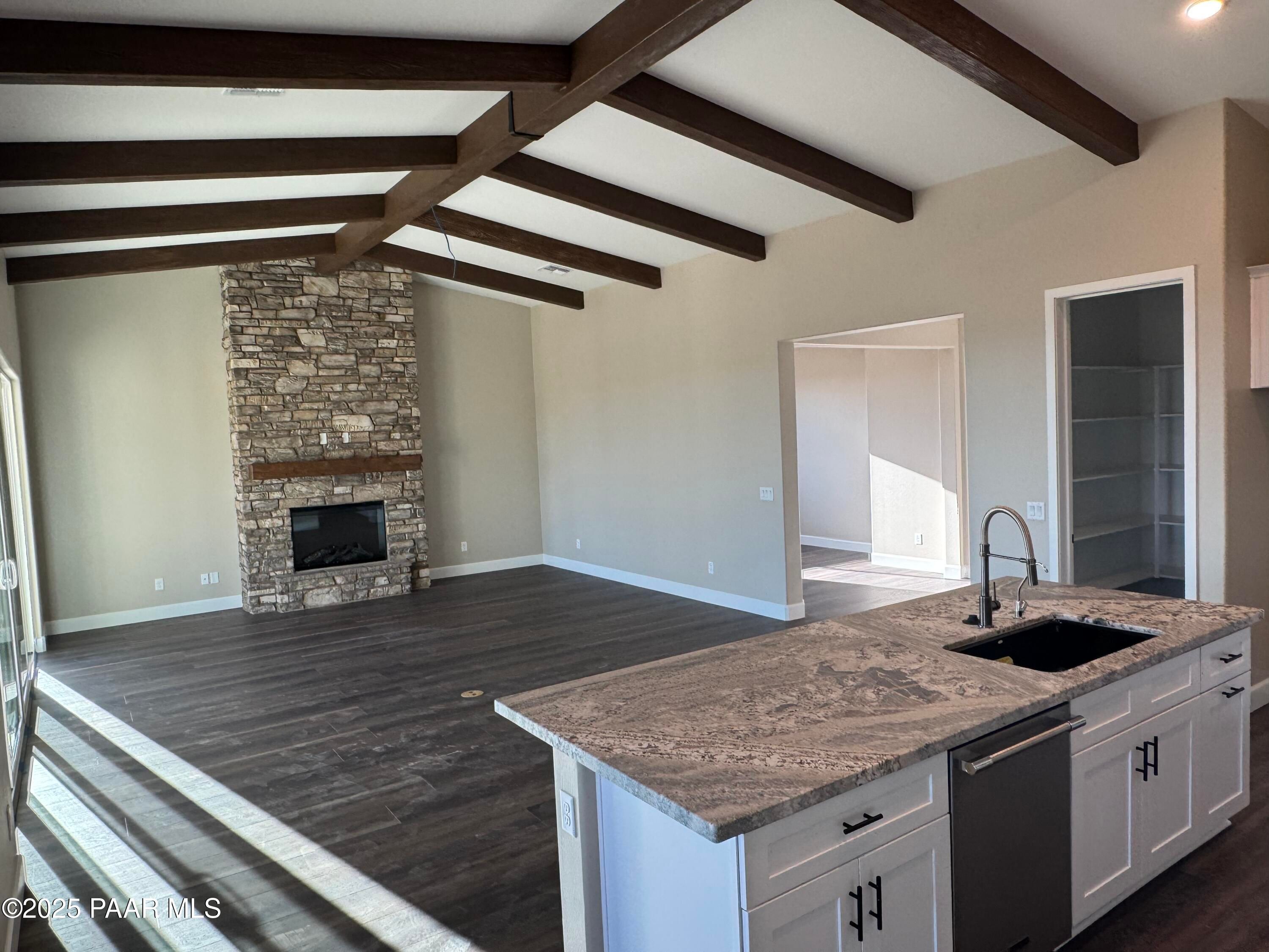 Open great room with stone fireplace, exposed wood beams, and large kitchen island in Evermore Homes Sunrise A, Prescott Valley, AZ