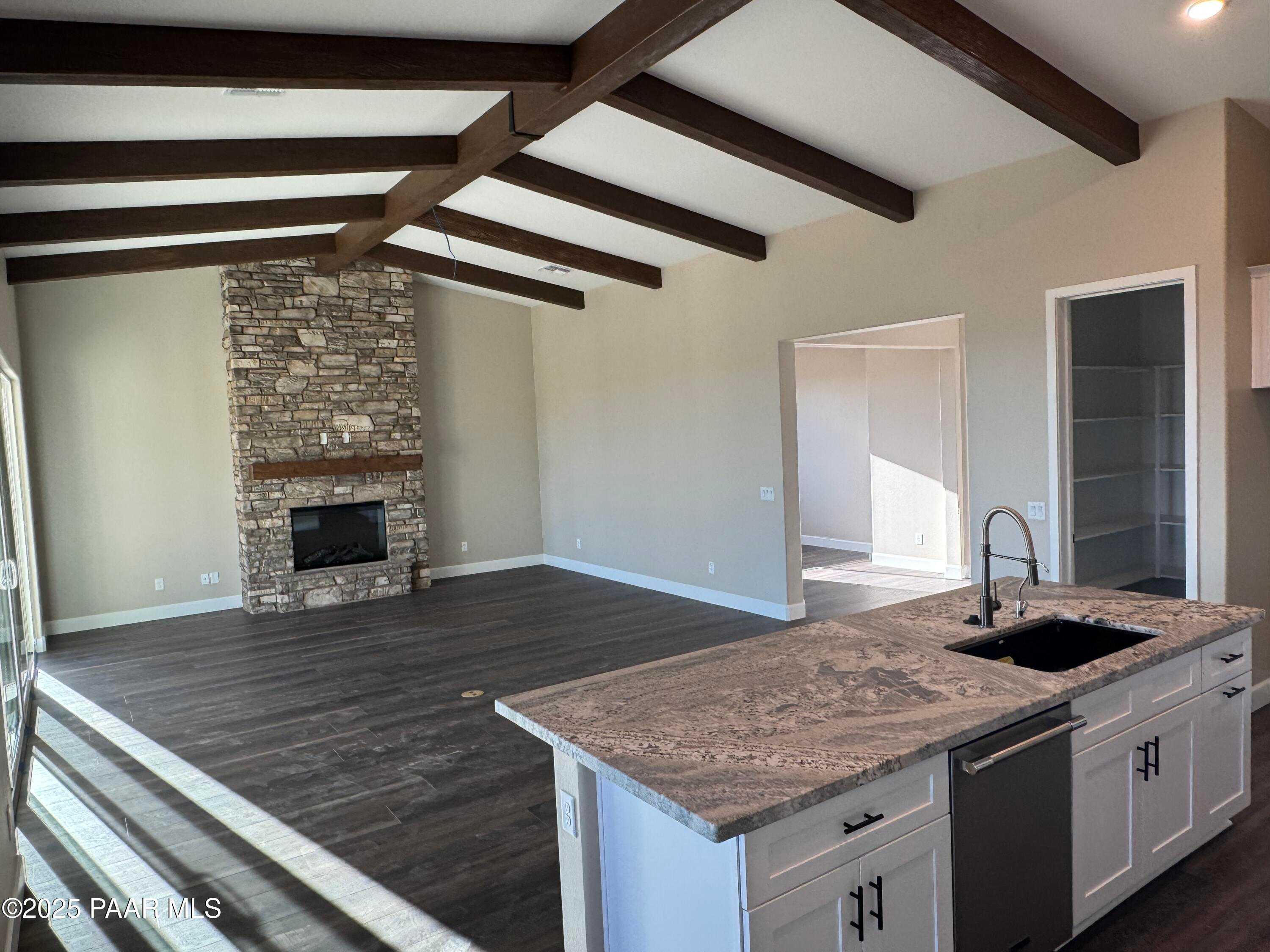Open great room with stone fireplace, exposed wood beams, and large kitchen island in Evermore Homes Sunrise A, Prescott Valley, AZ