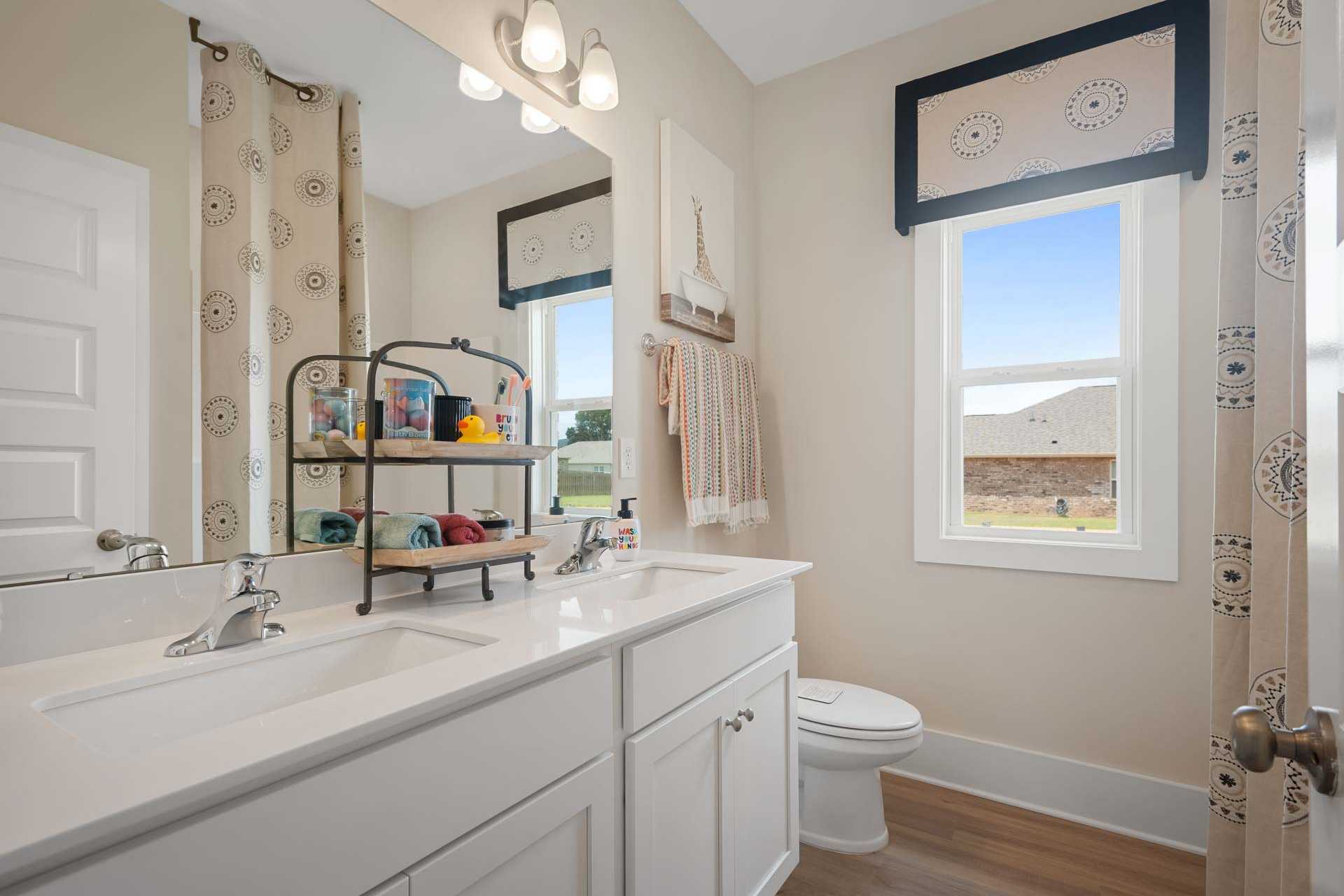 Spacious bathroom at Flint Meadows in New Market AL with double white vanity, large mirror, patterned shower curtain, and window view