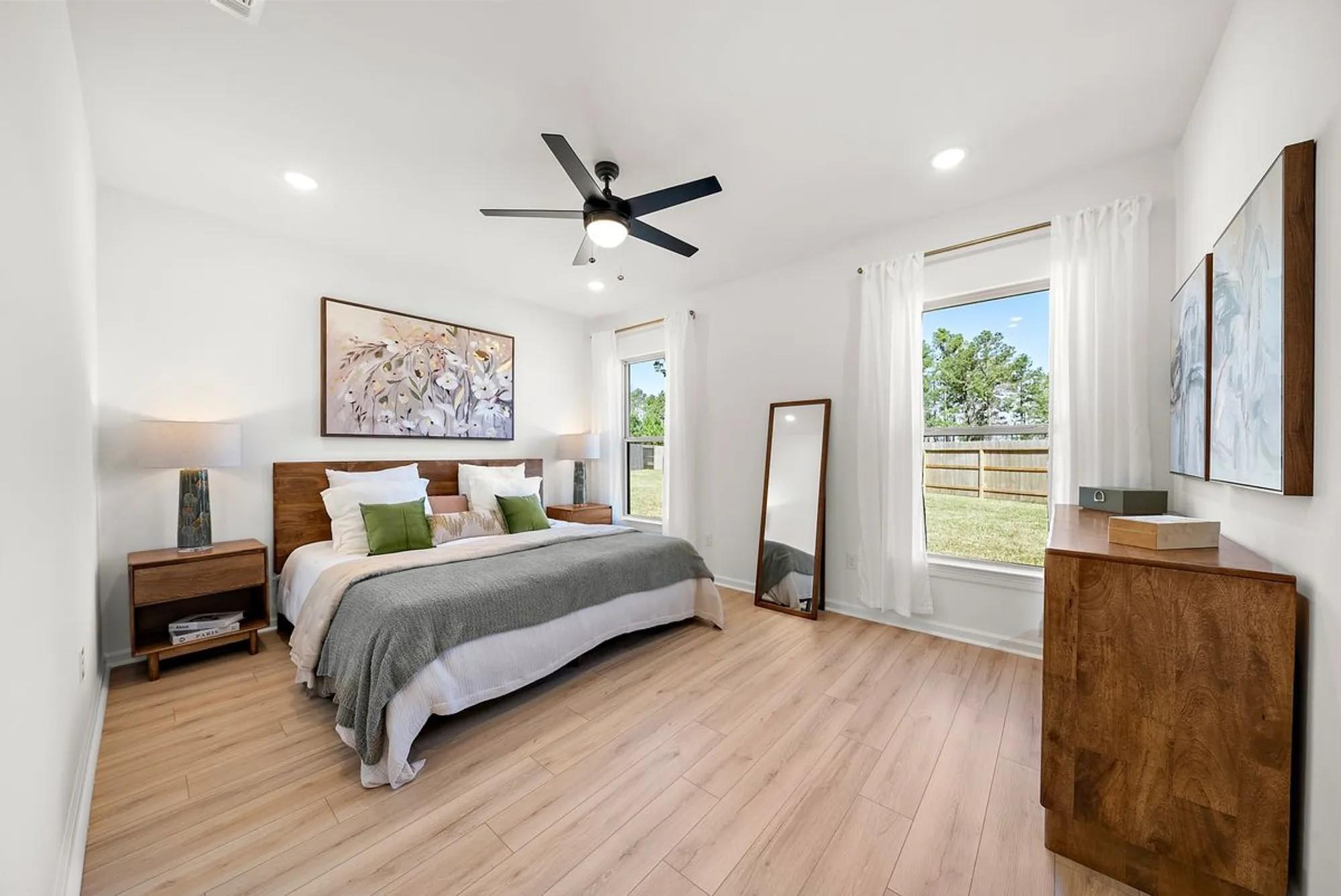 Modern master bedroom with king bed, ceiling fan, and backyard view window in Davidson Homes The Luna J, Sunterra, Katy, Texas