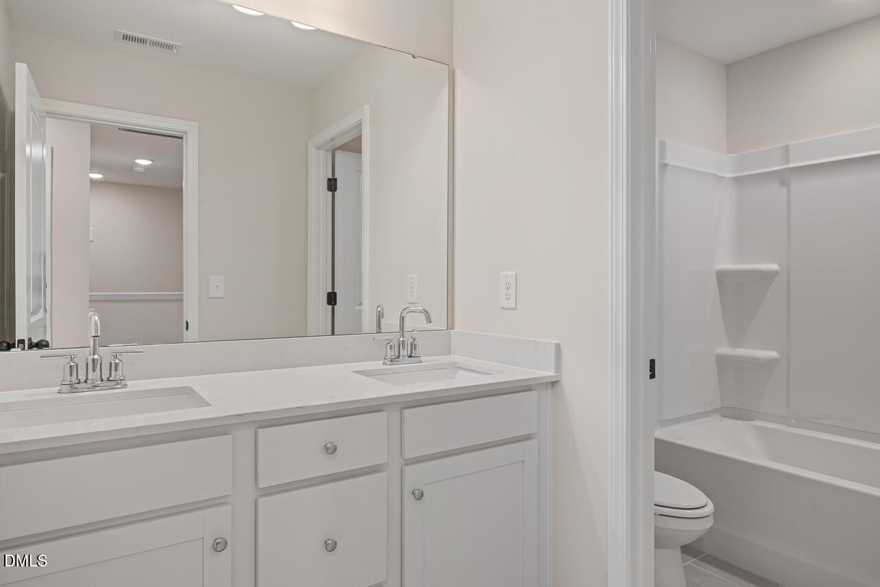 Spacious bathroom with double vanity, white quartz counters, soaking tub, and toilet in The Mitchell floor plan, Knightdale, NC
