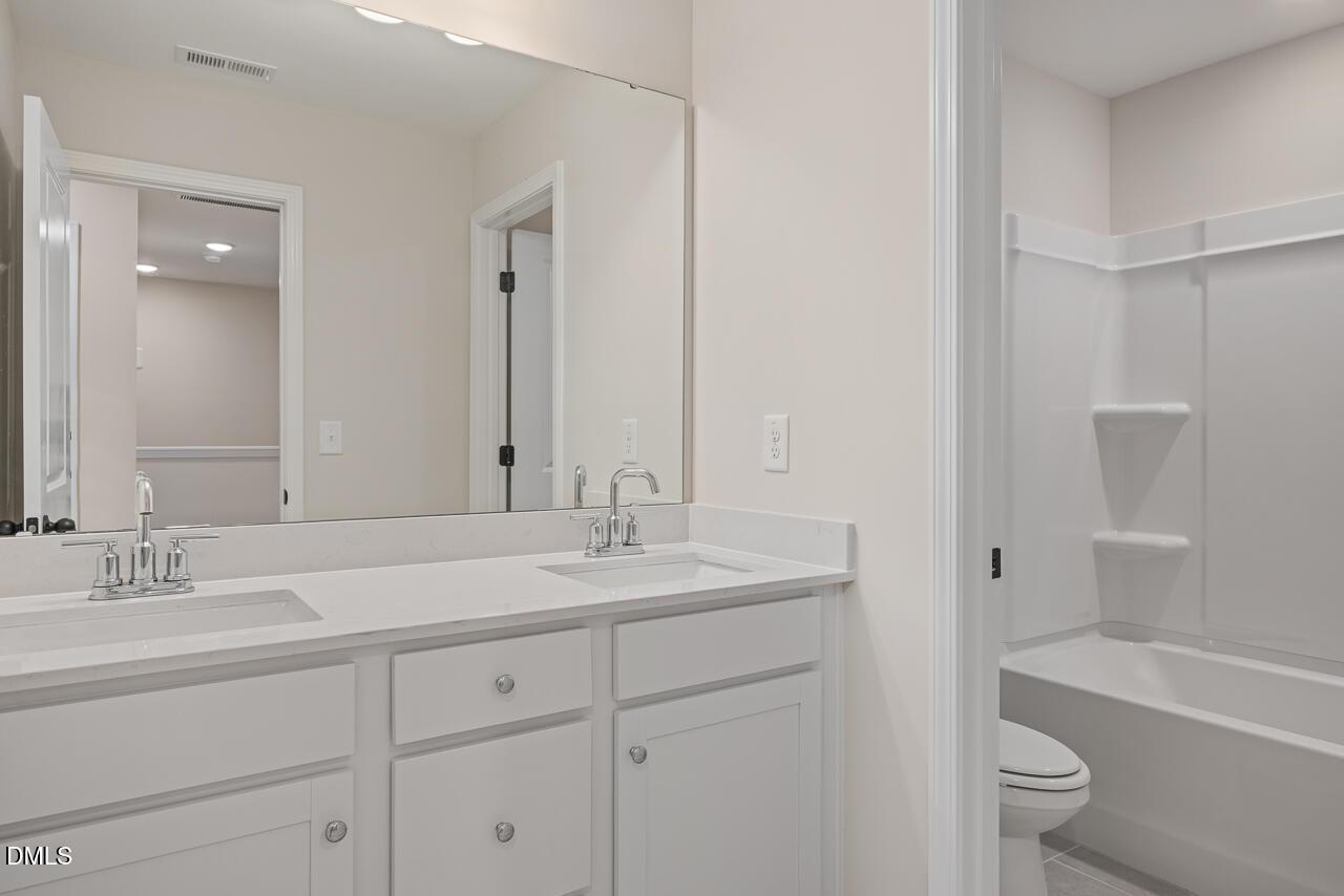 Spacious bathroom with double vanity, white quartz counters, soaking tub, and toilet in The Mitchell floor plan, Knightdale, NC