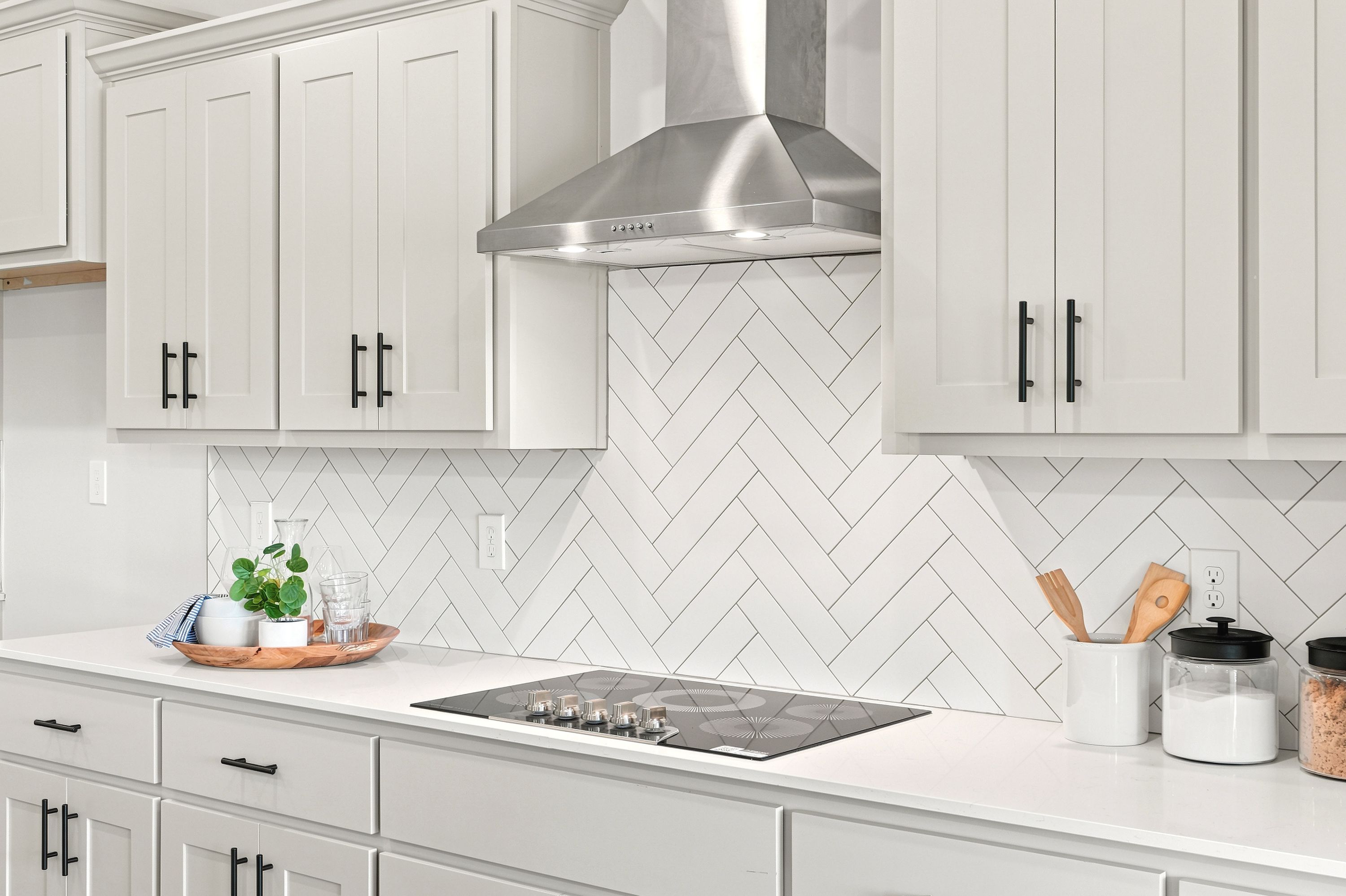 Modern kitchen at Riverton Preserve in Huntsville, AL featuring white shaker cabinets, herringbone backsplash, and cooktop.