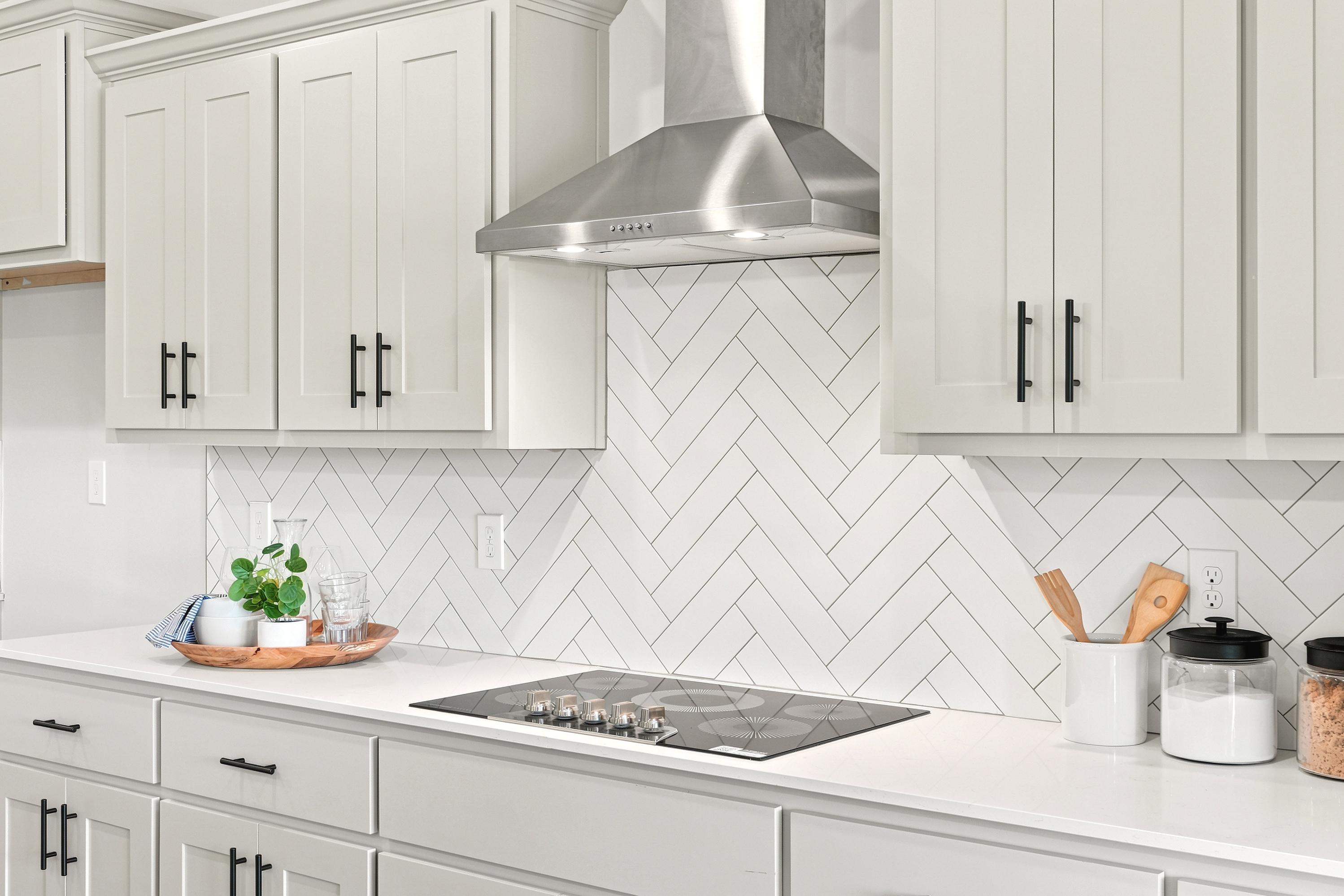 Modern kitchen at Riverton Preserve in Huntsville, AL featuring white shaker cabinets, herringbone backsplash, and cooktop.
