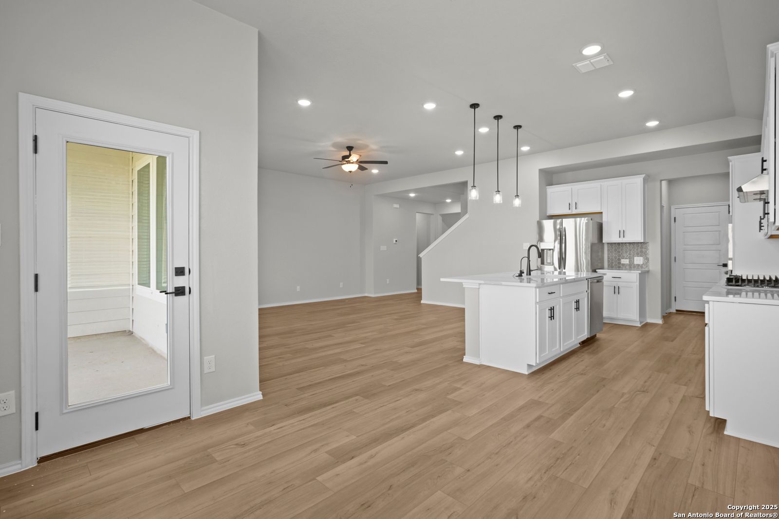 Open-concept kitchen with white island, stainless sink, pendant lights, and hardwood floors in The Sequoia A, Converse, Texas