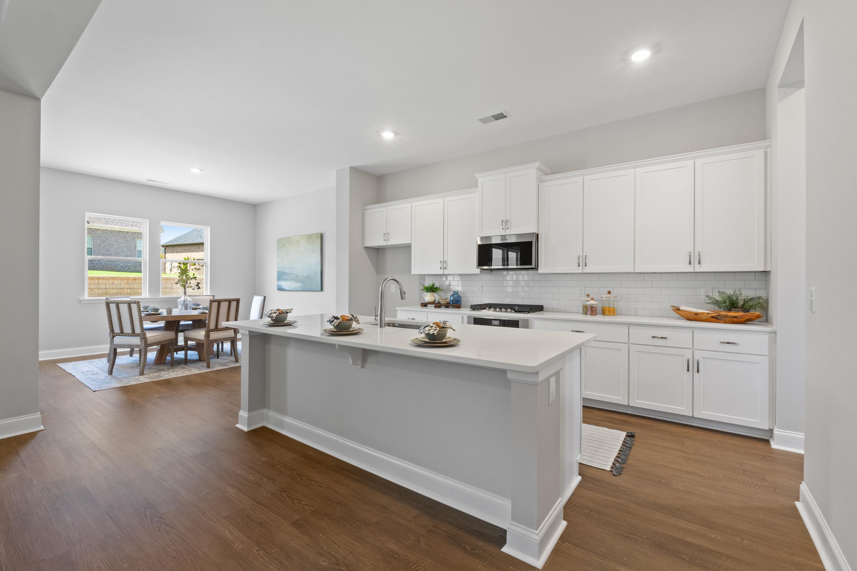 Open-concept kitchen and dining in The Haven D by Evermore Homes featuring white cabinets, large island, and hardwood floors