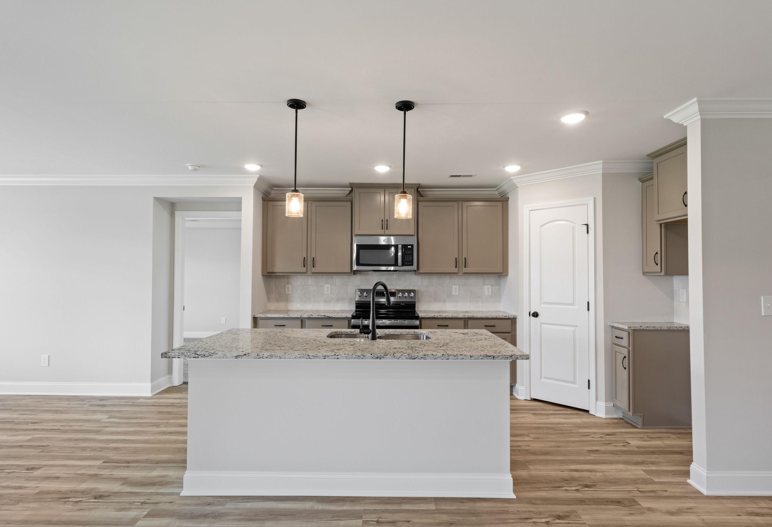 Modern kitchen in The Holly C featuring a granite island, taupe cabinetry, pendant lighting, and stainless appliances.