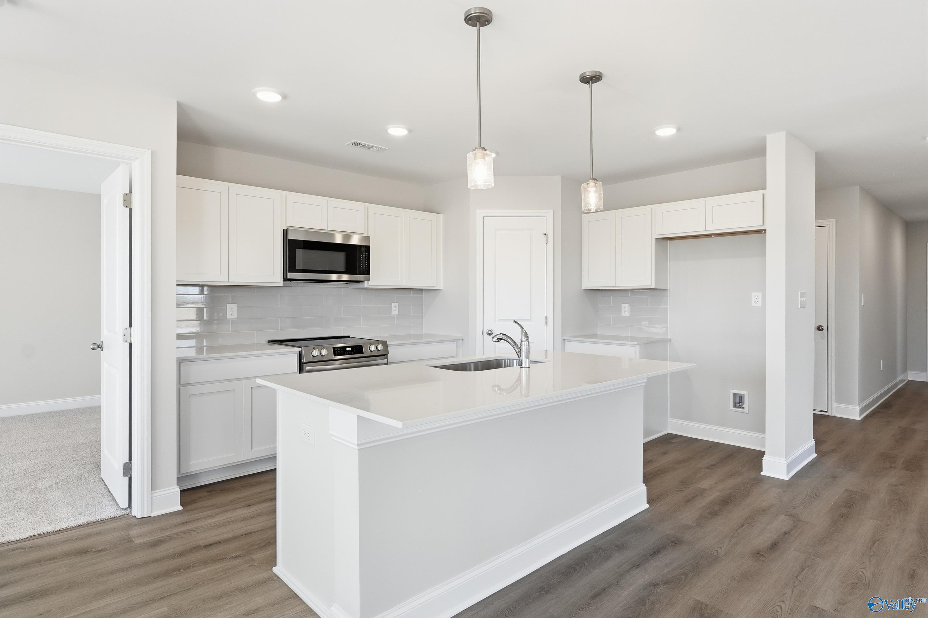 Modern white kitchen with island sink, stainless microwave, and open layout in Davidson Homes The Franklin, New Market, Alabama