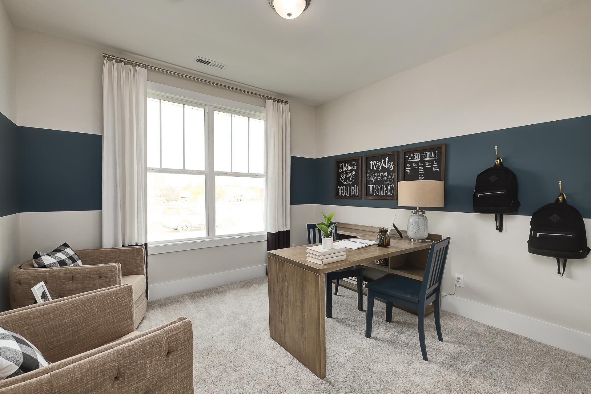 Cozy home office in The Everett with wooden desk, navy accent wall, black backpacks, and motivational signs