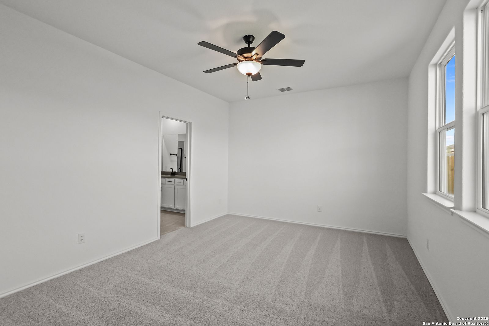 Bright bedroom with ceiling fan, white walls, carpet floor, and en-suite bathroom in Davidson Homes The Douglas E, San Antonio