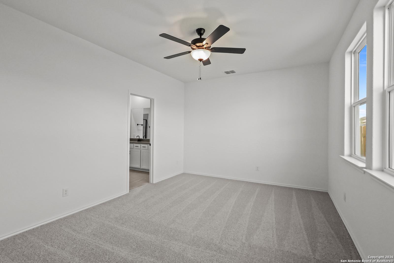 Bright bedroom with ceiling fan, white walls, carpet floor, and en-suite bathroom in Davidson Homes The Douglas E, San Antonio