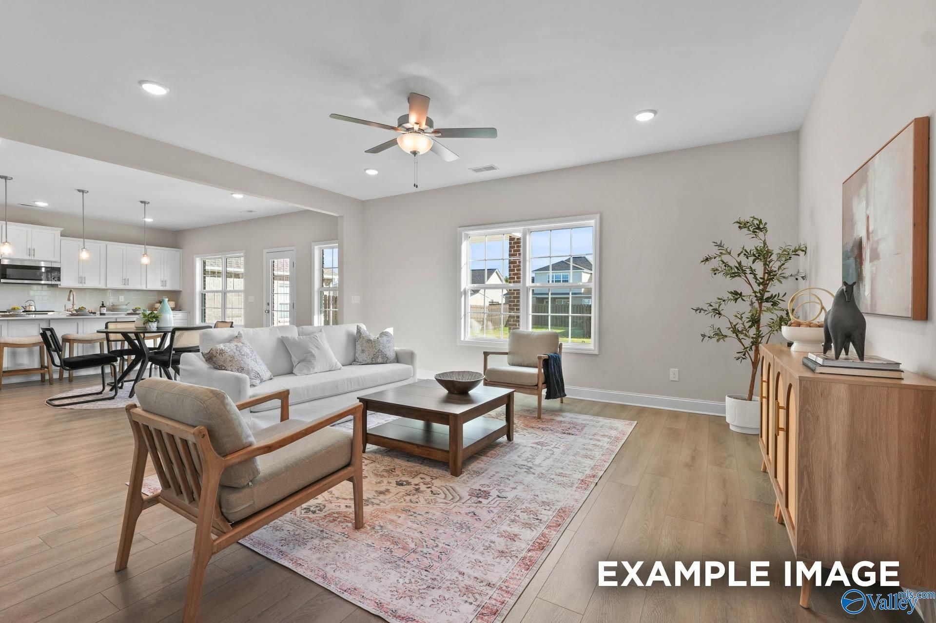 Open-concept living room with ceiling fan, large windows, and adjacent white kitchen in 5-bedroom Evermore Homes The Madison D, Madison, Alabama