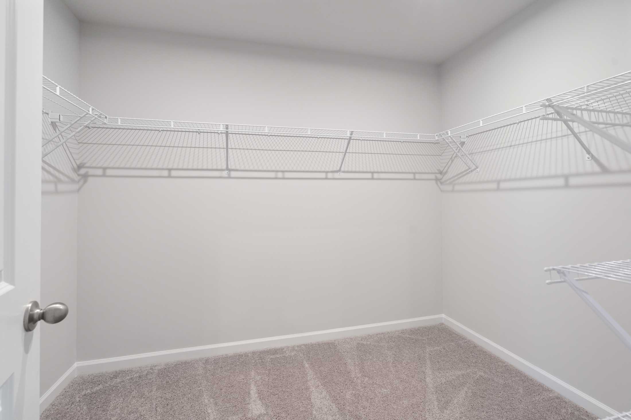 Spacious walk-in master closet in The Cary A with white wire shelving, beige carpet, and open door