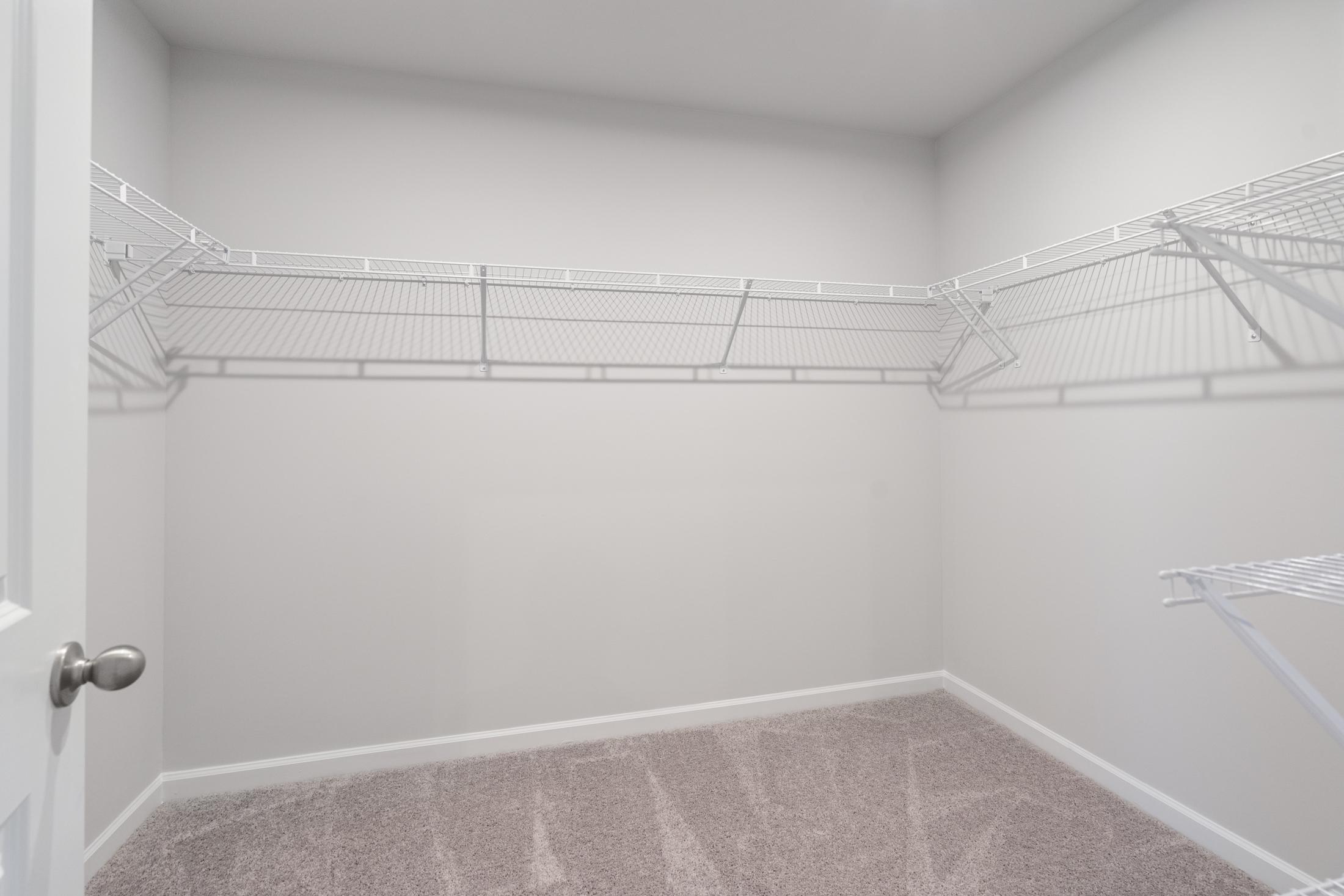 Spacious walk-in master closet in The Cary A with white wire shelving, beige carpet, and open door