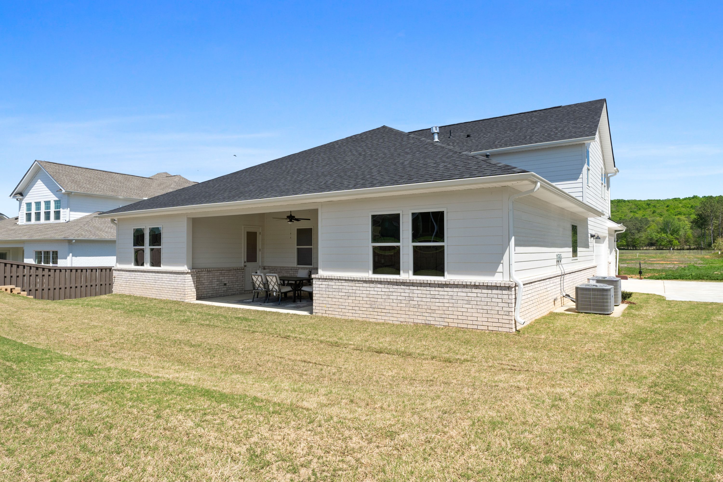 Side view of The Haven D 1-story home with covered patio, black shingle roof, white siding, and brick base in Owens Cross Roads