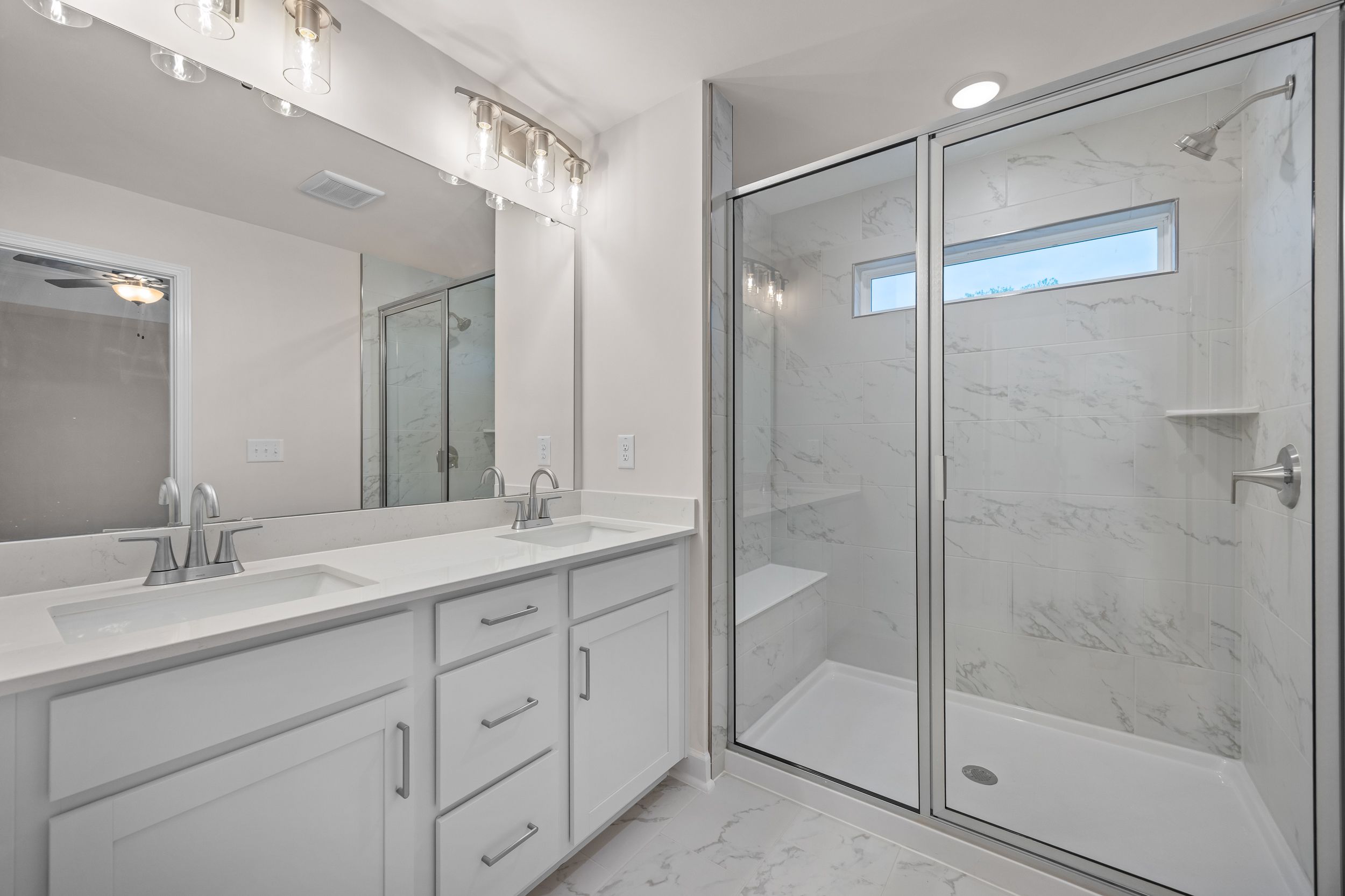 Luxury primary bathroom in Forestville Yard Townhomes, Knightdale NC: double white vanity, frameless glass shower, marble tiles