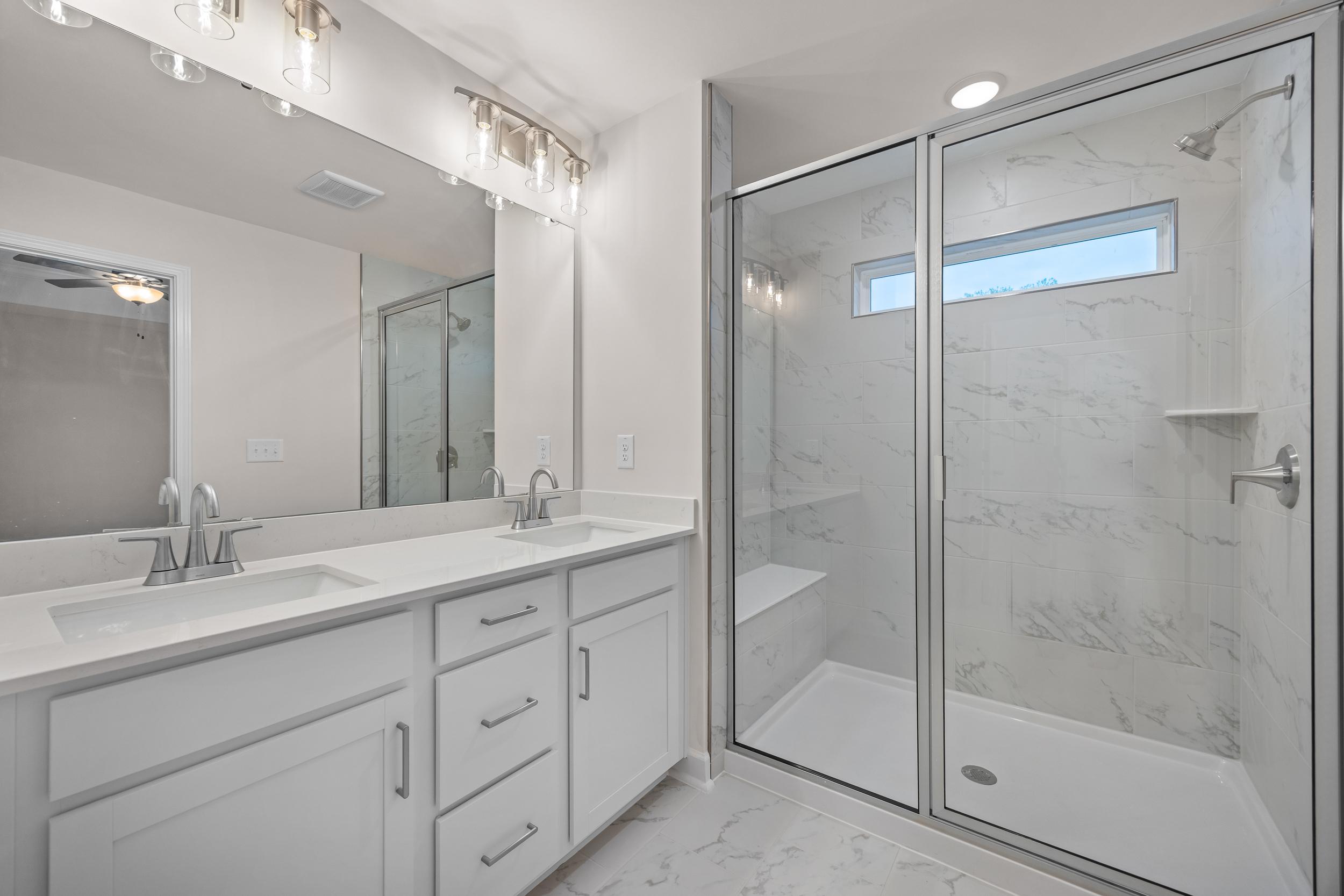 Luxury primary bathroom in Forestville Yard Townhomes, Knightdale NC: double white vanity, frameless glass shower, marble tiles