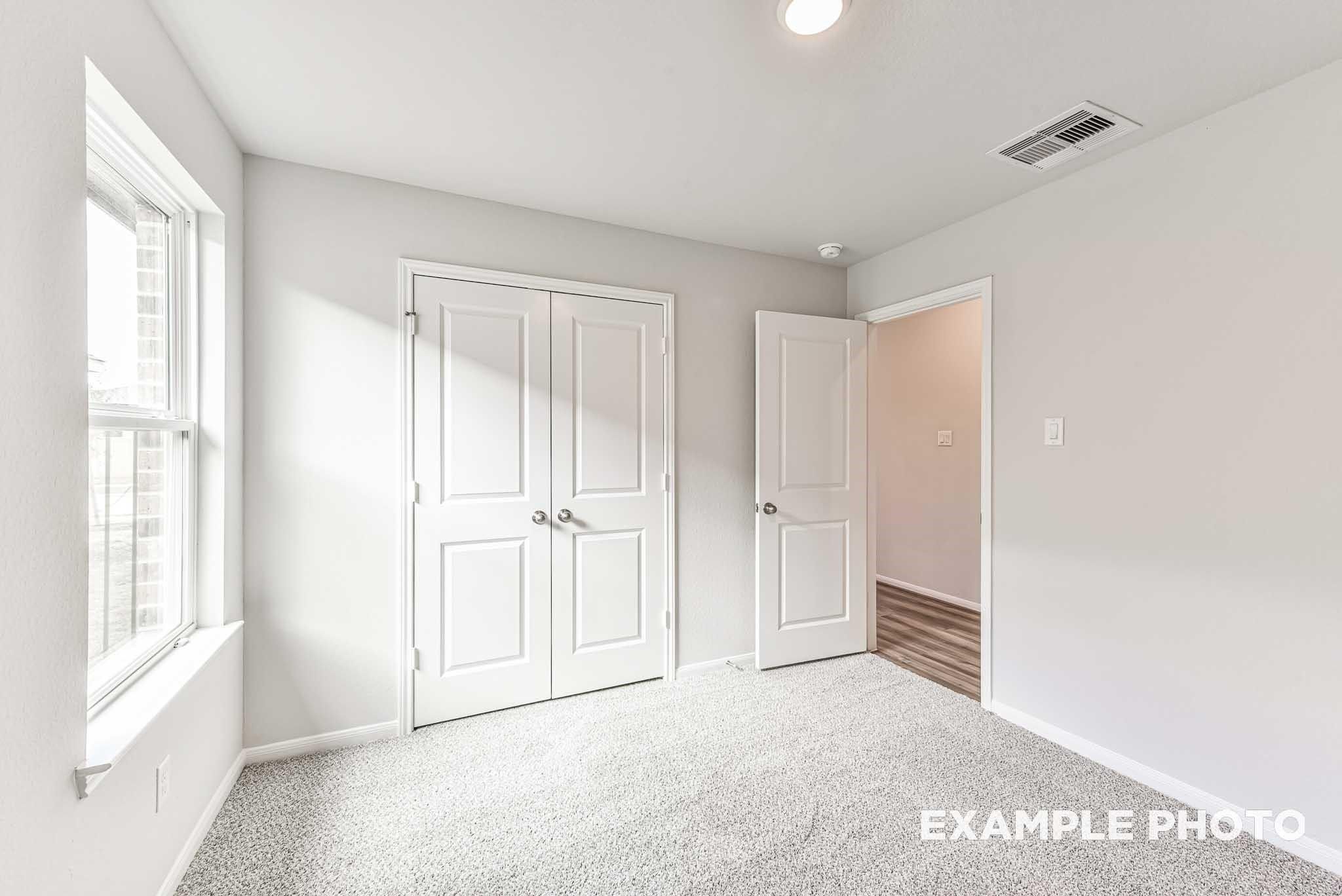 Bright bedroom with plush carpet, double-door closet, and neutral walls in The Laguna C floor plan, Sunterra, Katy, TX.