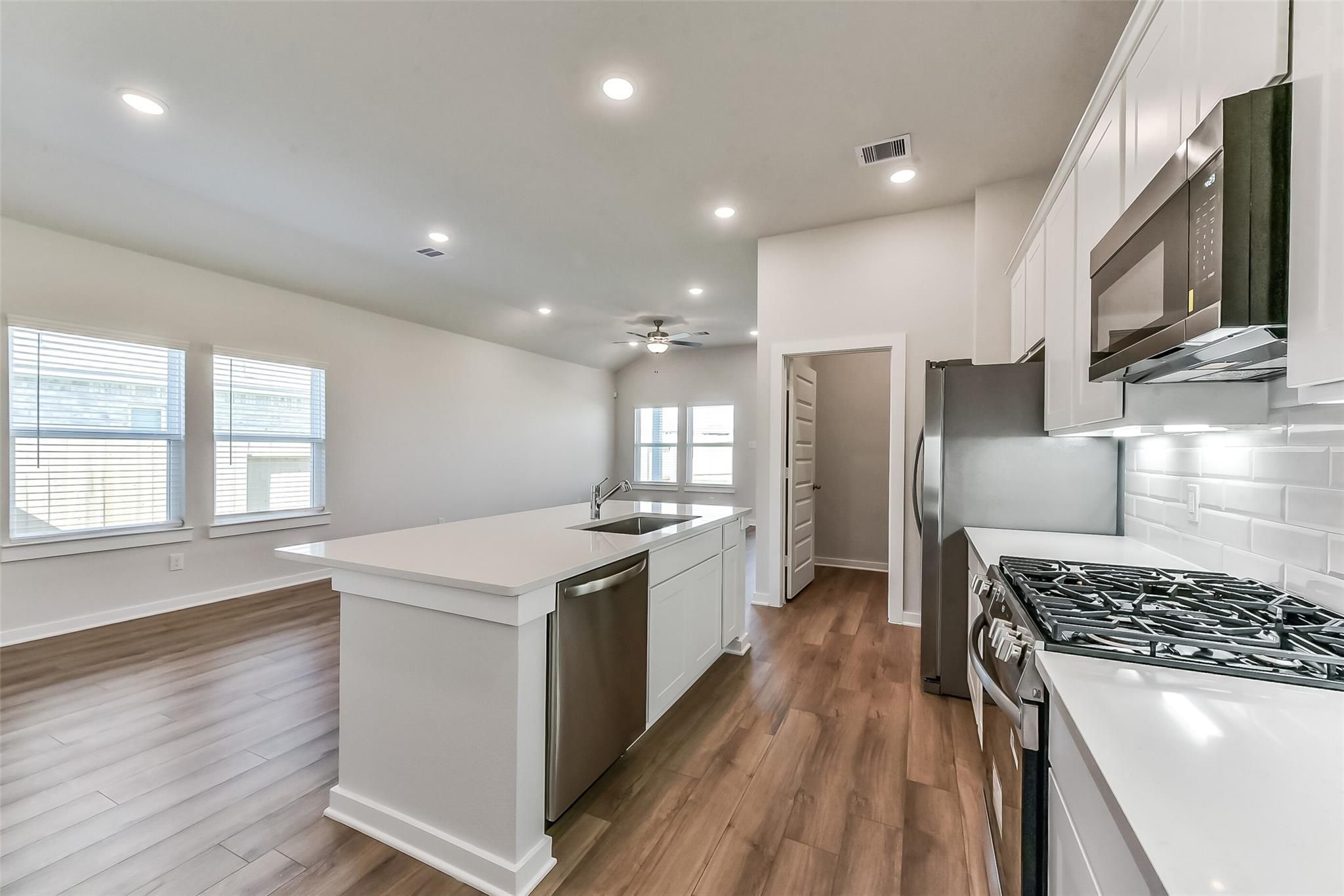 Modern open kitchen with white quartz island, stainless gas range, subway tile backsplash in Davidson Homes The Costa B, Dayton TX