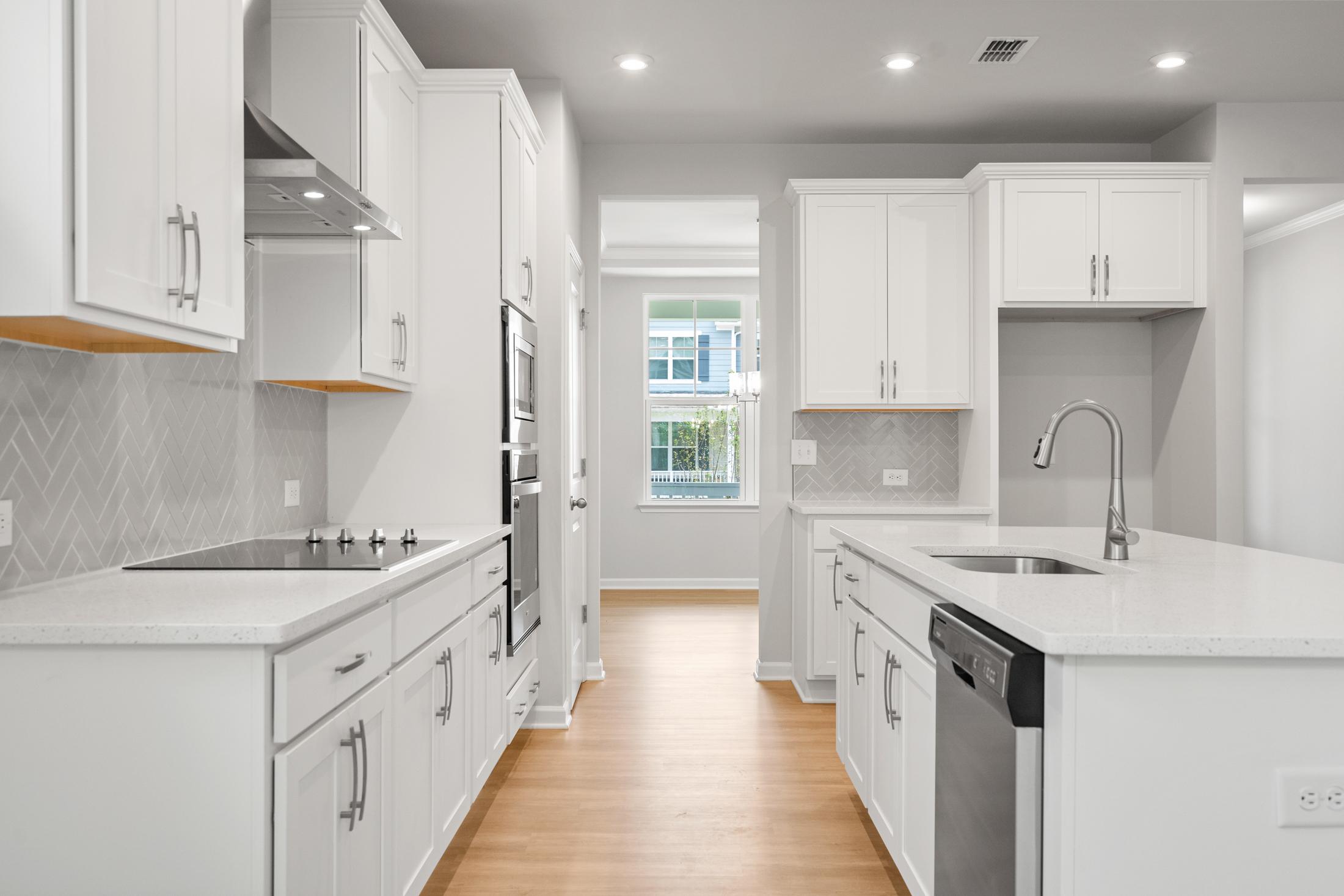 Modern kitchen in The Ash B at Wehunt Meadows featuring white cabinets, subway tile backsplash, quartz island, and stainless appliances