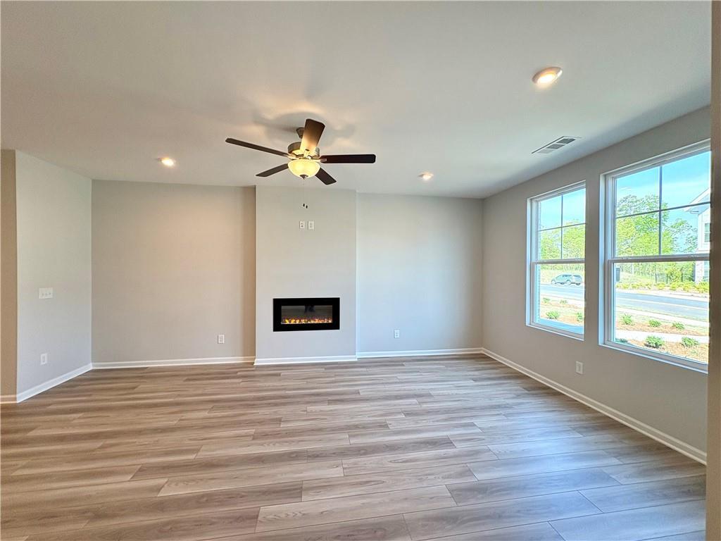 Spacious living room with modern gas fireplace, ceiling fan, hardwood floors, and large windows in Davidson Homes The Monroe A, Emerson, GA