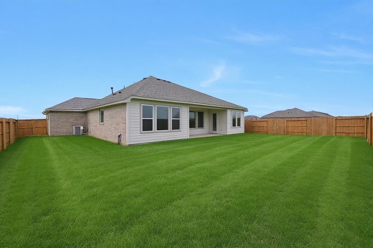 Single-story beige brick home with covered patio, large windows, and 3-car garage in fenced green backyard, Lago Mar, Texas City