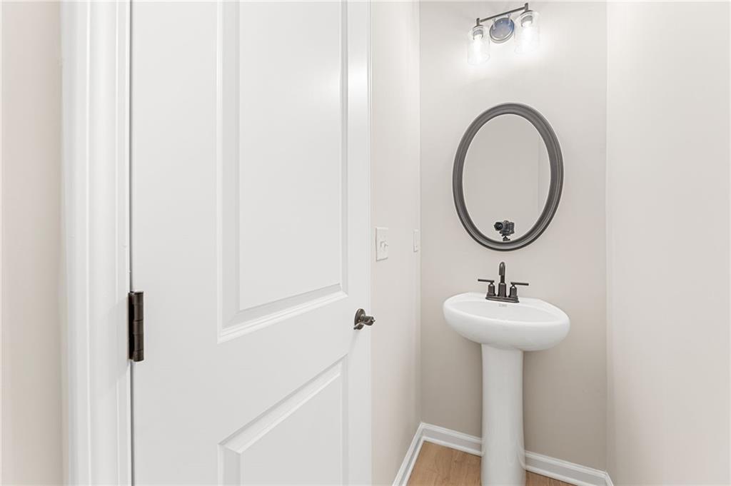 Elegant powder room featuring white pedestal sink, round mirror, and soft lighting in Davidson Homes The Glenwood C, Loganville, GA