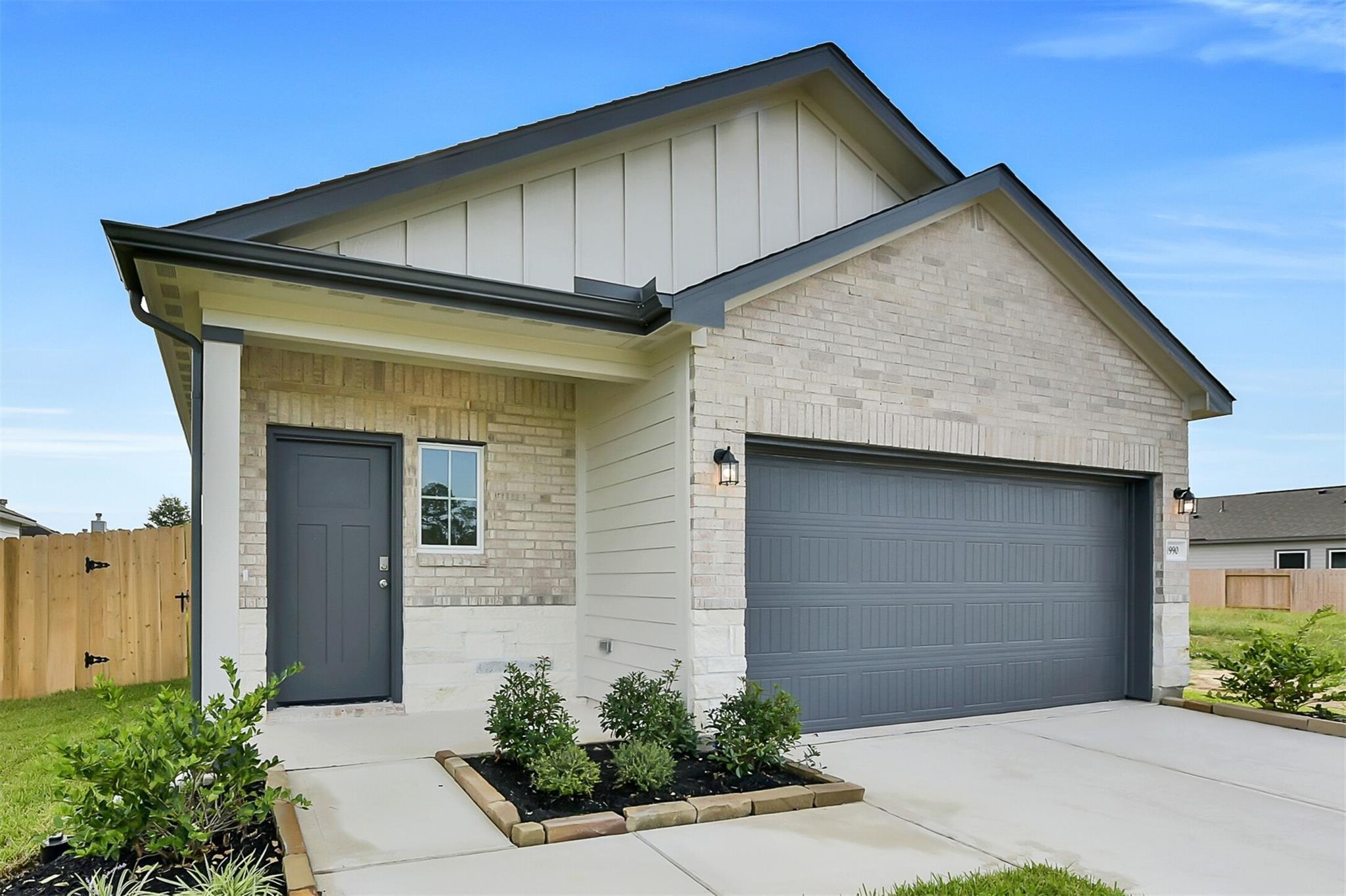 Modern beige brick single-story home with gray roof, 2-car garage, and landscaped entry in Dayton, Texas