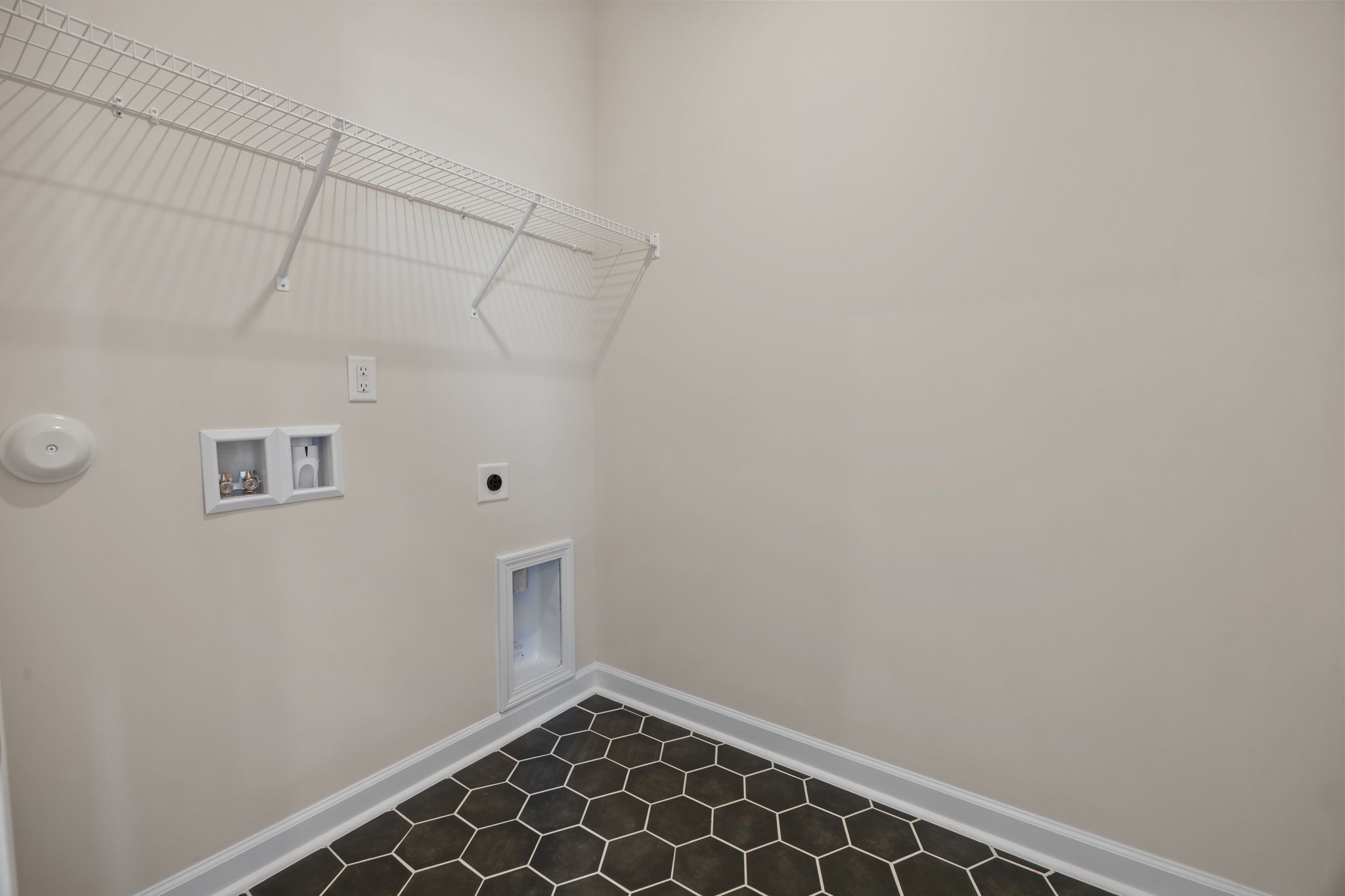 Laundry room with hexagon tile flooring and wire shelving at Forestville Yard in Knightdale, NC by Davidson Homes.