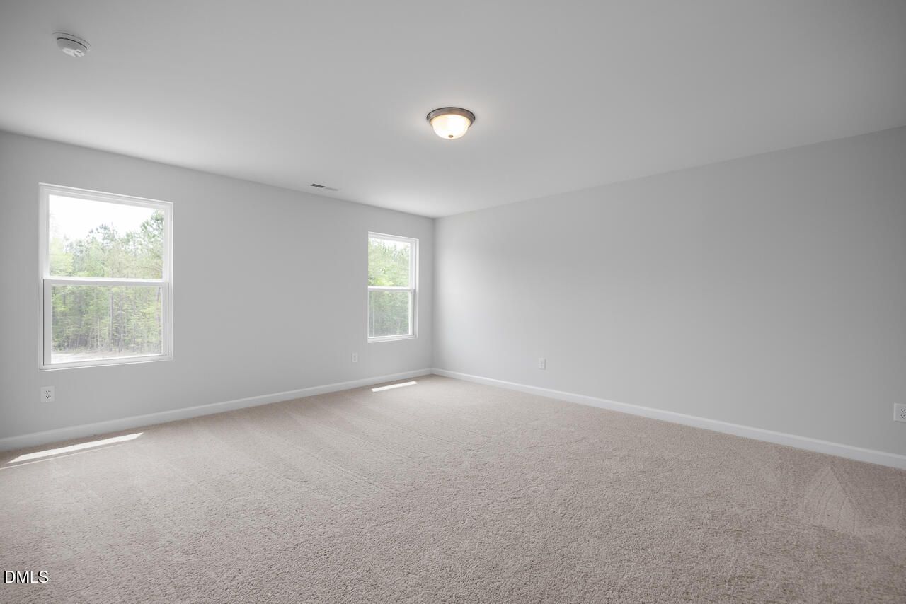 Empty bedroom with light gray walls, beige carpet, double windows overlooking trees in 5-bedroom Davidson Homes The Hickory II B, Zebulon, NC