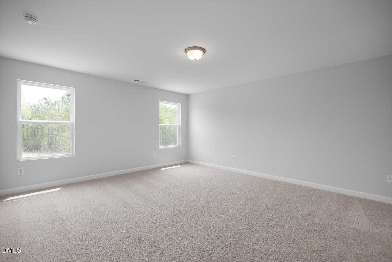 Empty bedroom with light gray walls, beige carpet, double windows overlooking trees in 5-bedroom Davidson Homes The Hickory II B, Zebulon, NC