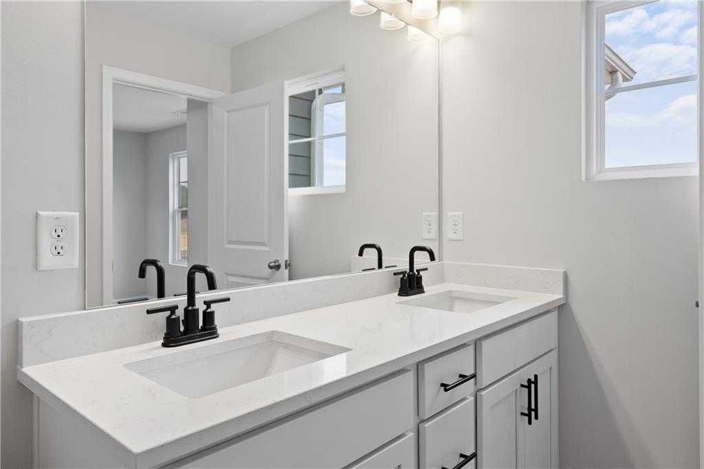 Modern double vanity bathroom with white quartz counters, black faucets, and large mirror in Davidson Homes The Durant A, Emerson, GA