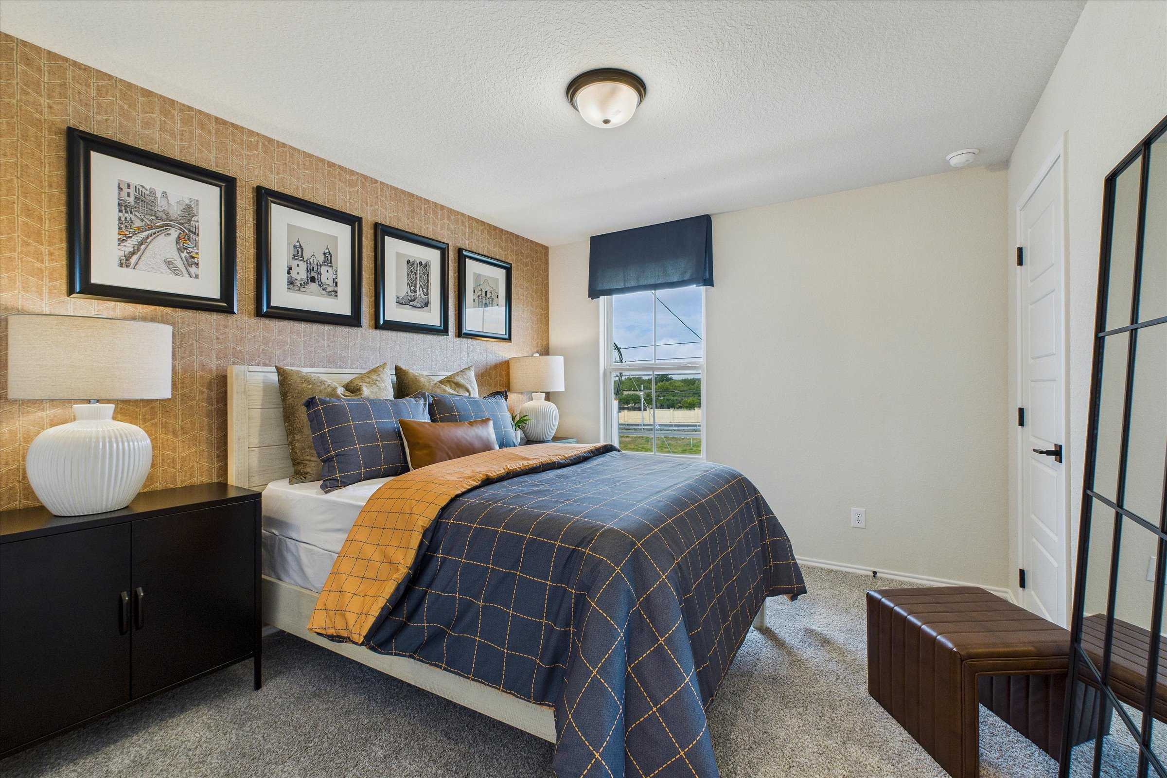 Cozy bedroom interior at Meadows at Oak Creek in San Antonio Texas with blue plaid bedding, beige walls, and framed artwork