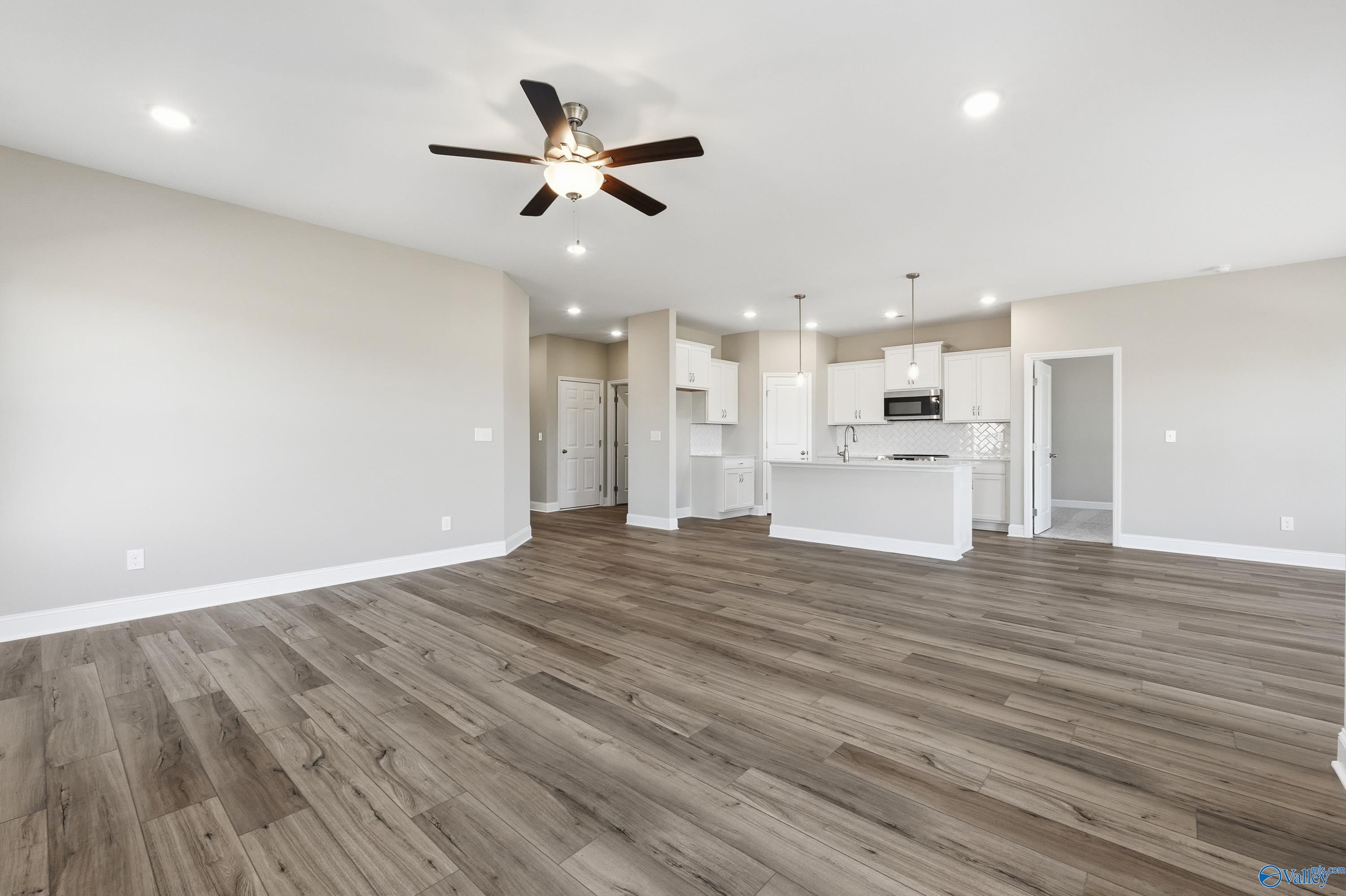 Open-concept kitchen and living area with wood floors, white cabinets, stainless appliances, and ceiling fan in Davidson Homes The Franklin C, New Market, Alabama